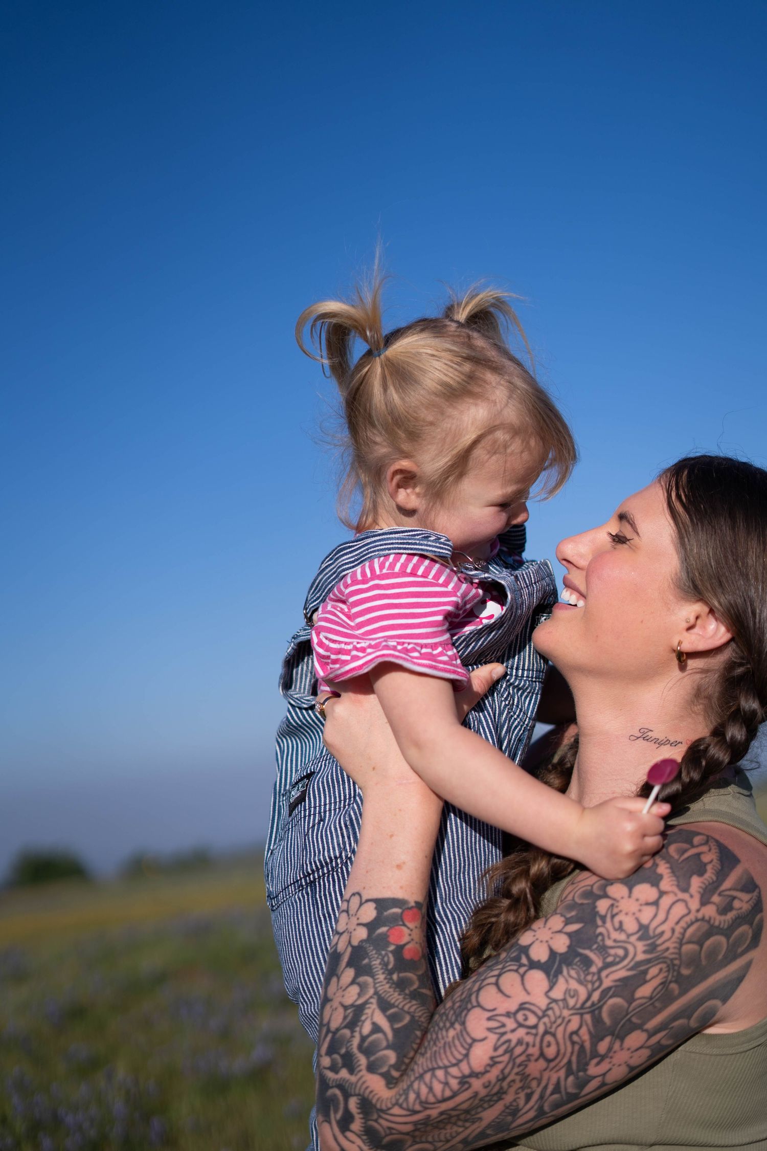 Joyful interaction between adult with tattoos and toddler in striped shirt outdoors.