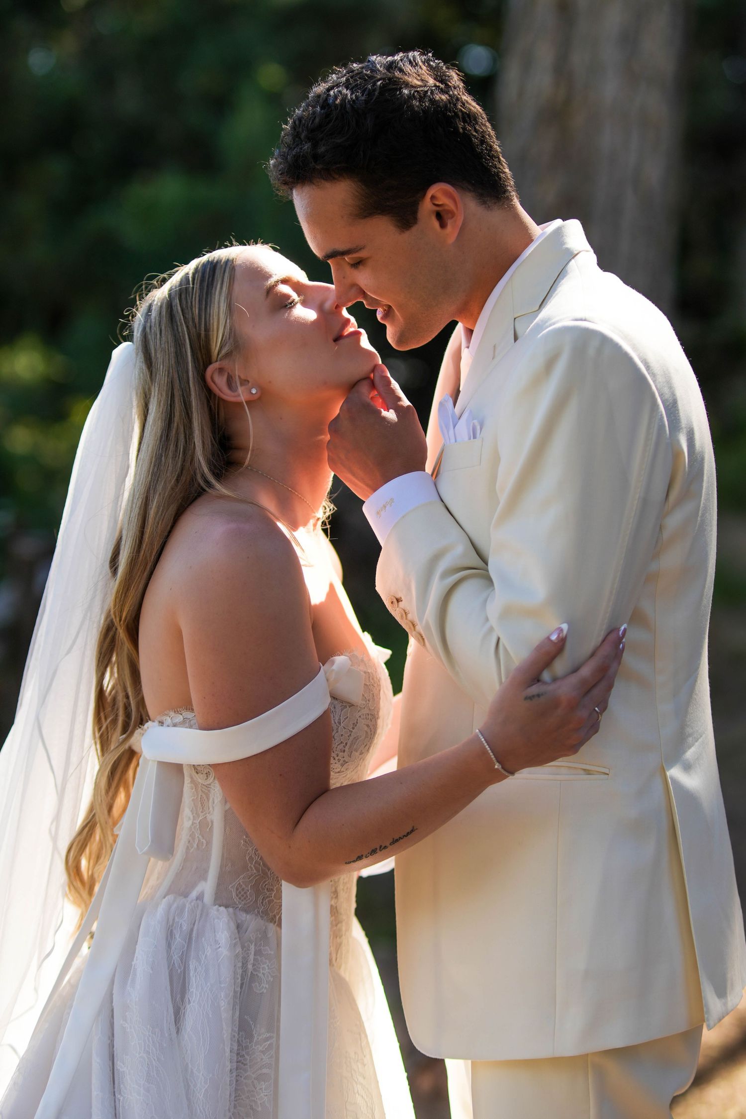 Bride and groom share a romantic moment outdoors, with the groom gently lifting the bride's chin for a kiss.