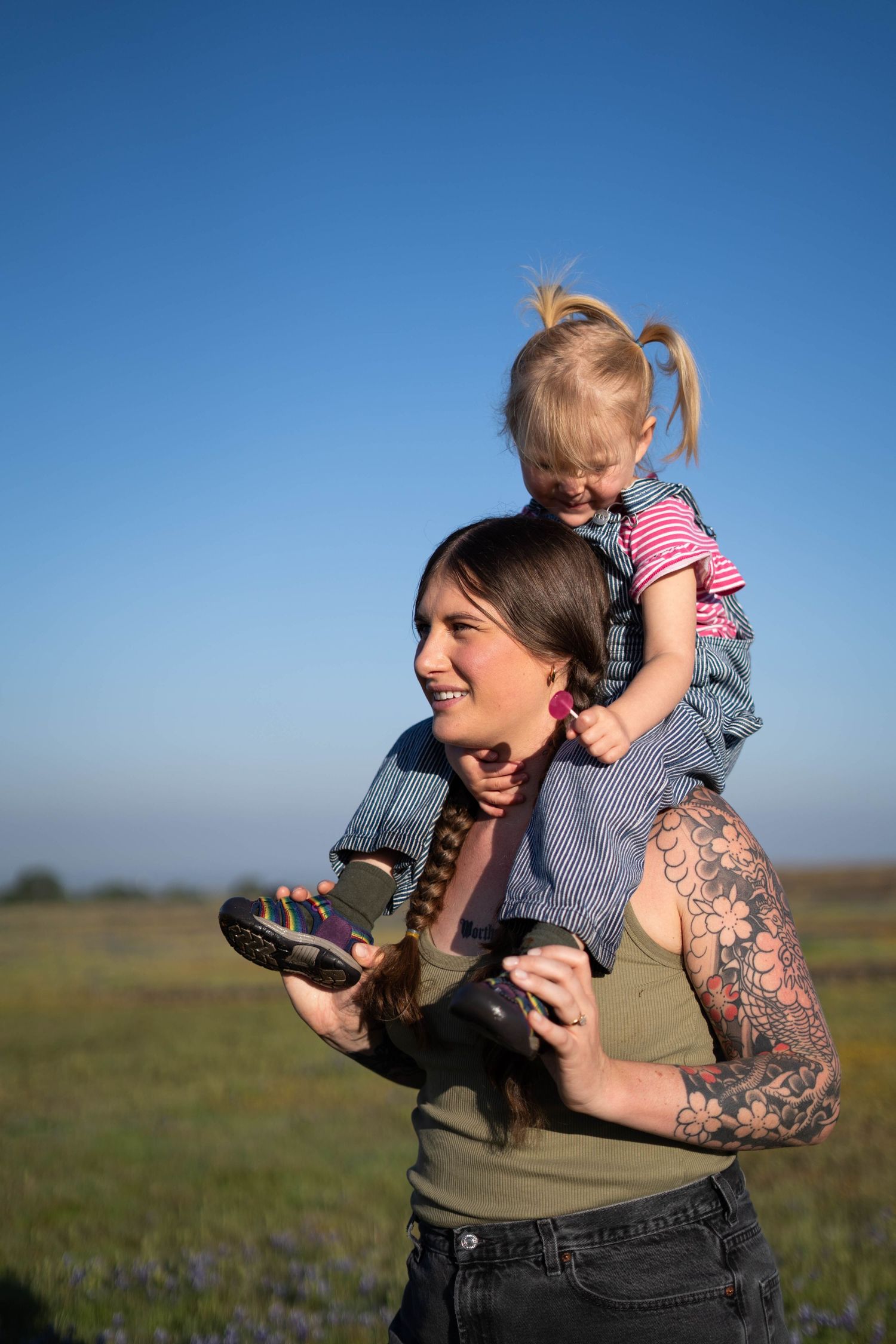 Candid moment of adult lifting child in air against blue sky and grassy field.