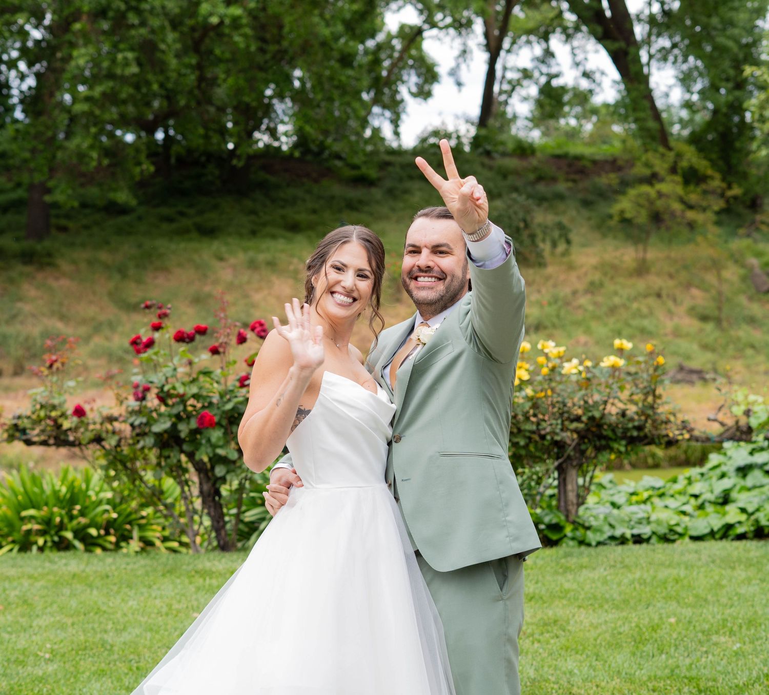 Newlyweds celebrating with joyful gestures in a garden surrounded by summer flowers.