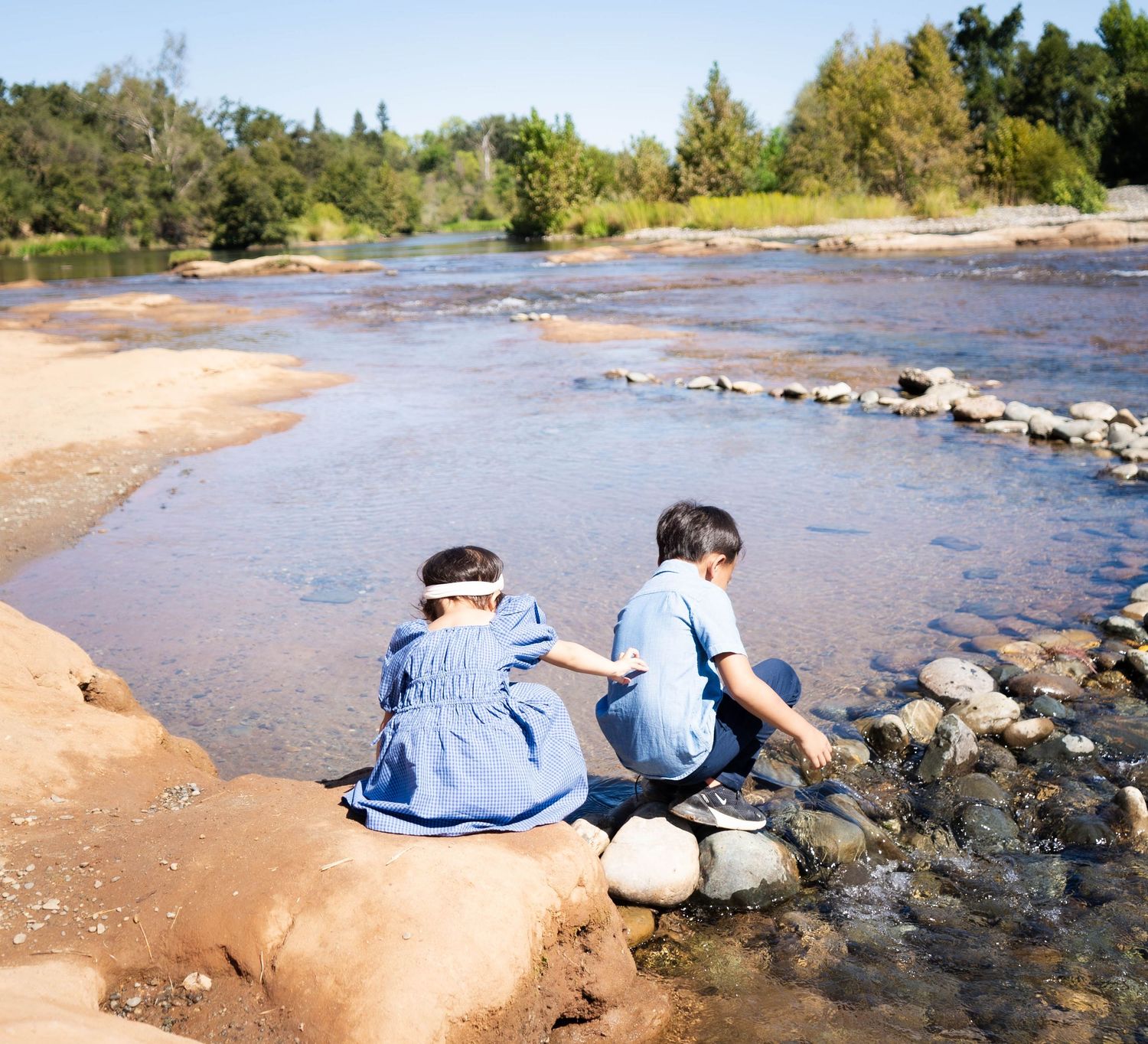 People sitting on rocky riverbank enjoying scenic view of flowing water.