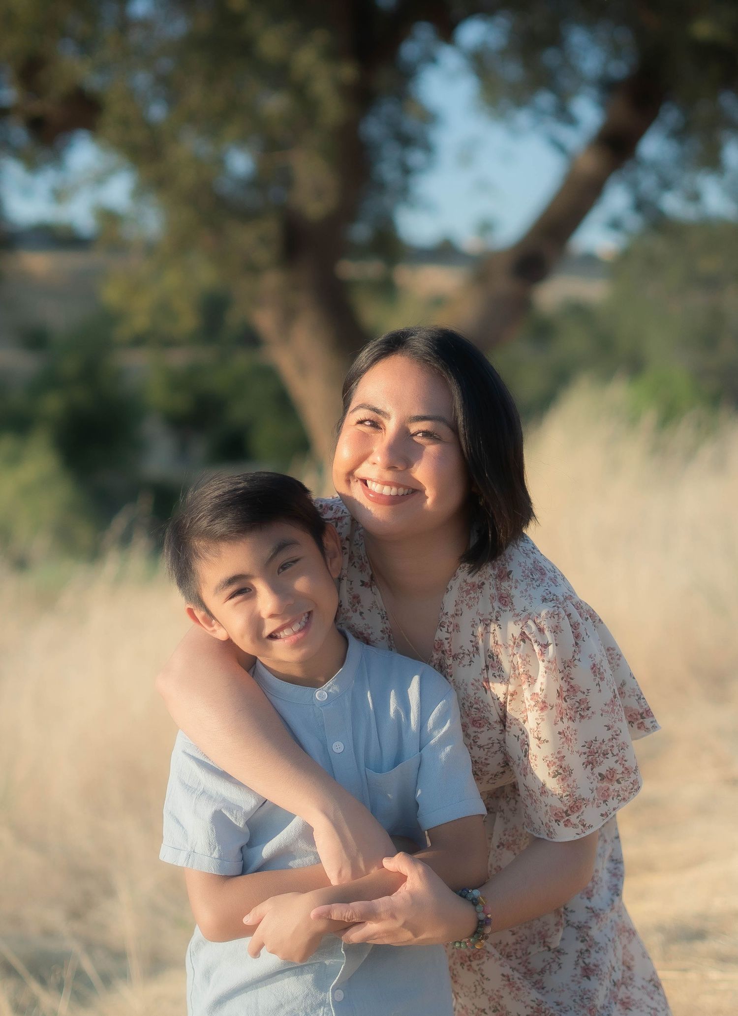 Two people share a warm embrace while posing in golden sunlit field.
