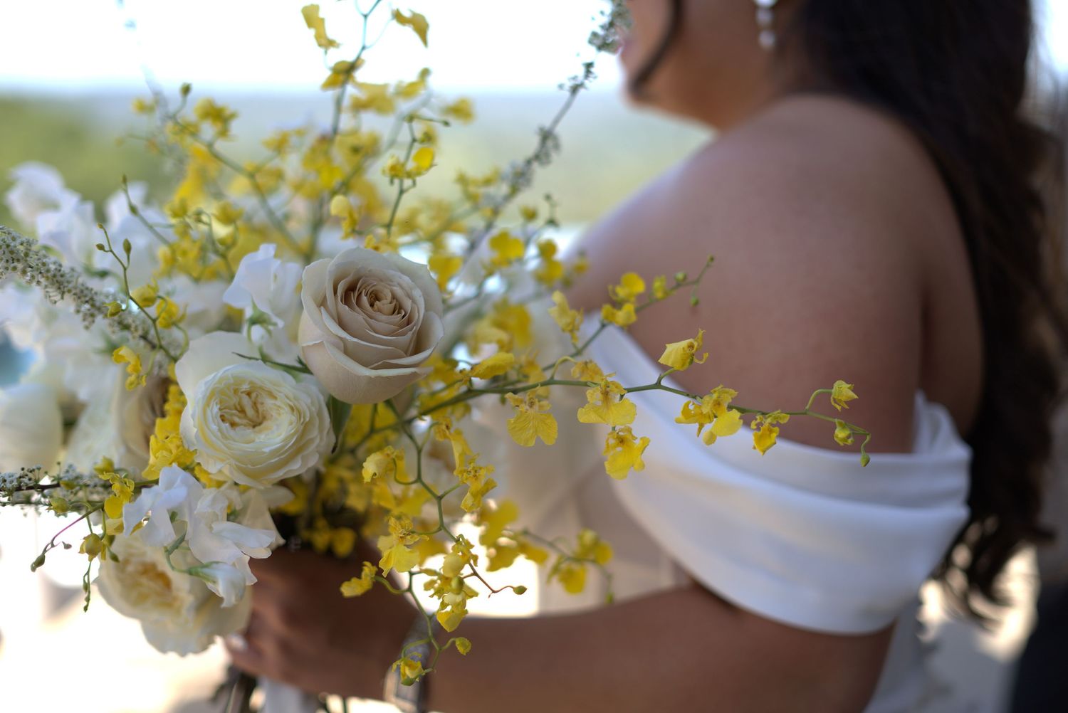 Wedding bouquet details featuring white roses and yellow orchids in natural sunlight.