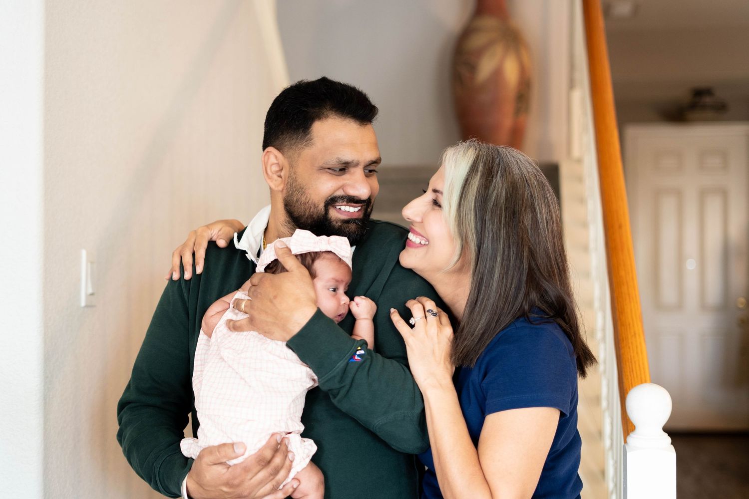 Happy couple smiling at their newborn baby indoors, new parents sharing a joyful moment with infant.