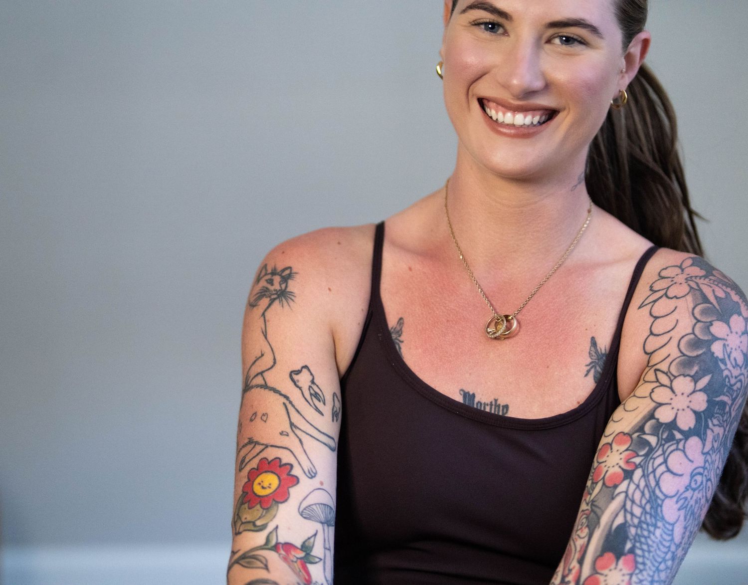 Person in black tank top with colorful sleeve tattoos and necklace smiling.