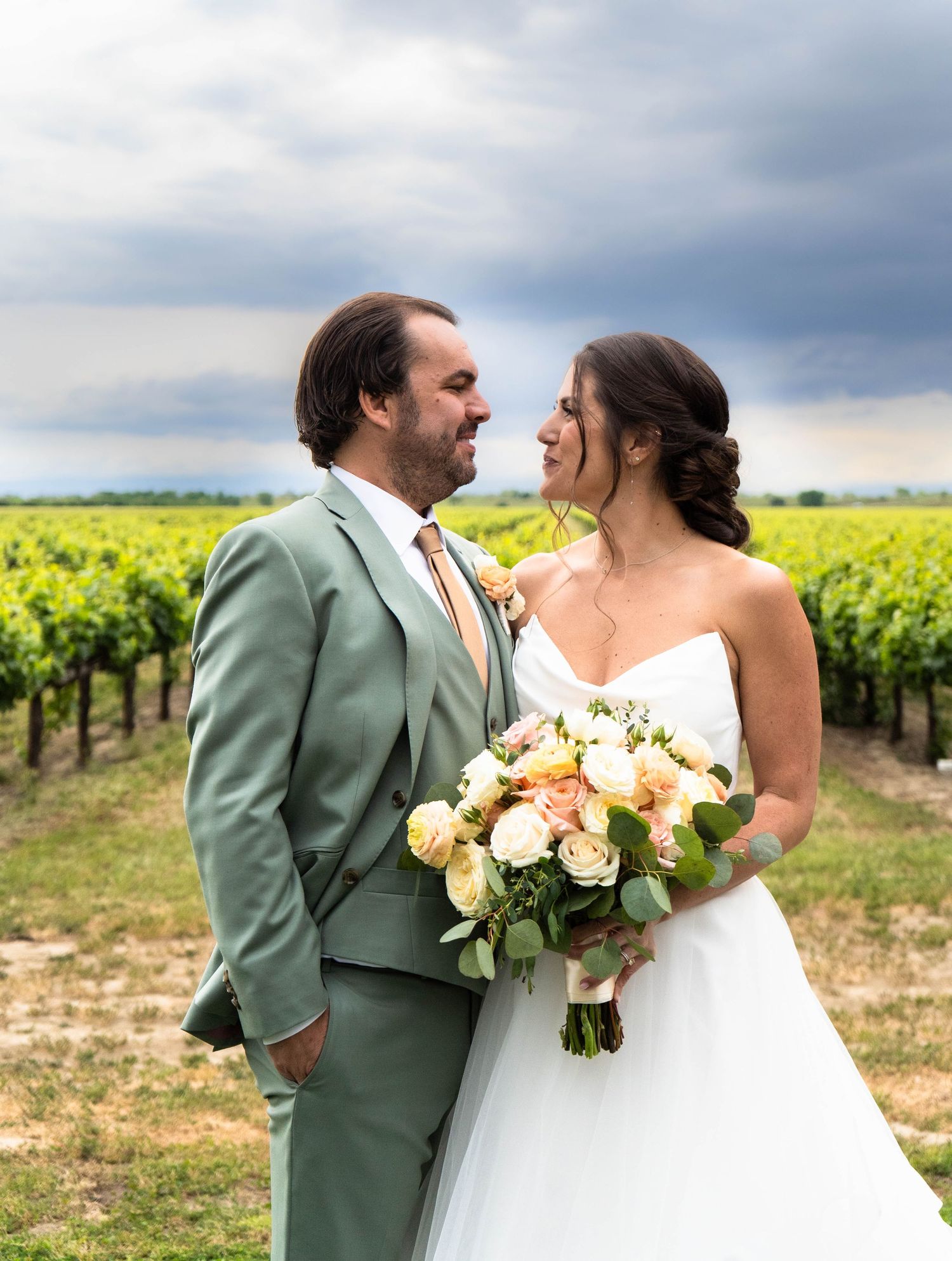 Newlyweds share intimate moment in vineyard with yellow floral bouquet.