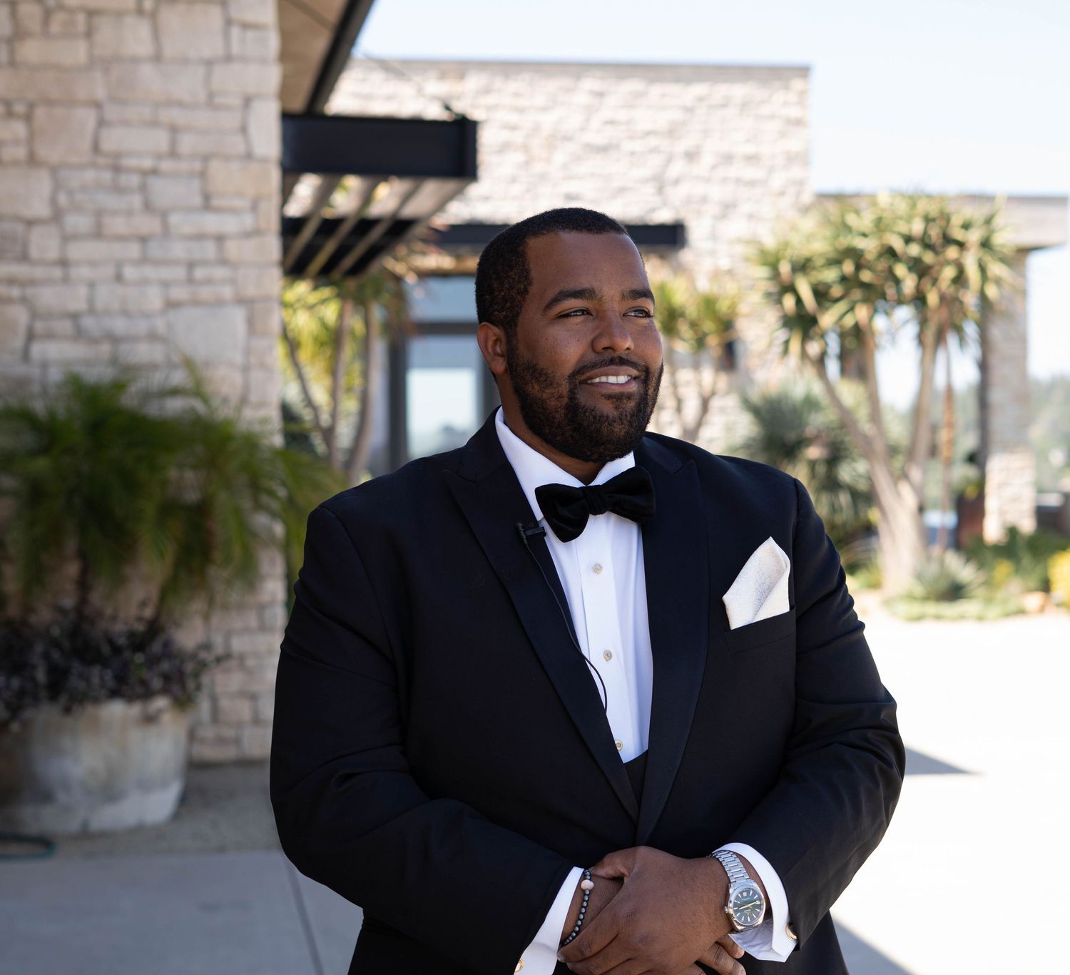 Groomsmen in formal attire sharing laughs outside stone building.