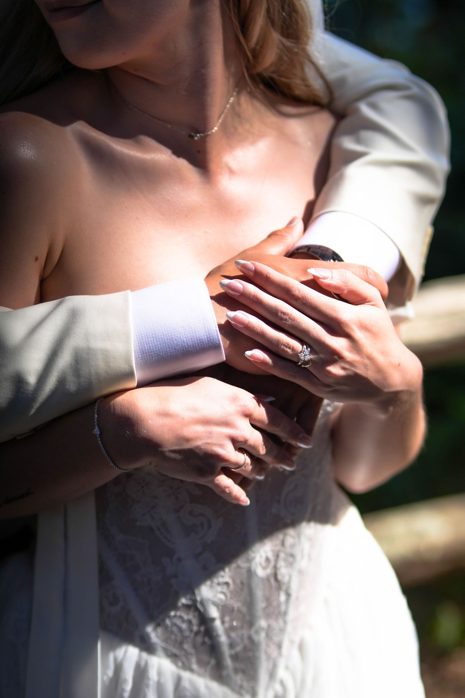 Bride and groom holding hands together, showing wedding rings, in an intimate outdoor embrace on their wedding day.