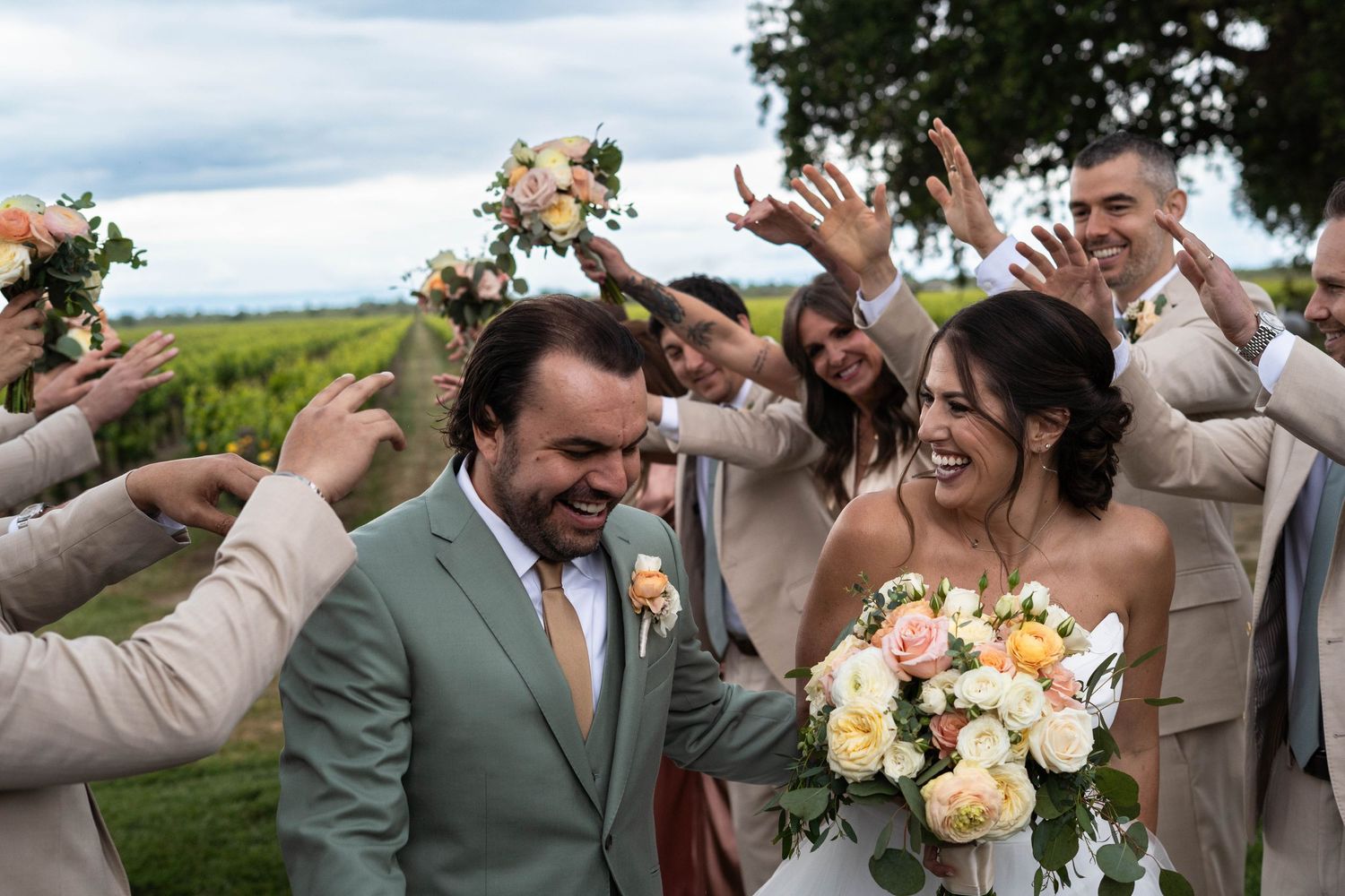 Wedding party celebrating with enthusiastic gestures against a vineyard landscape.
