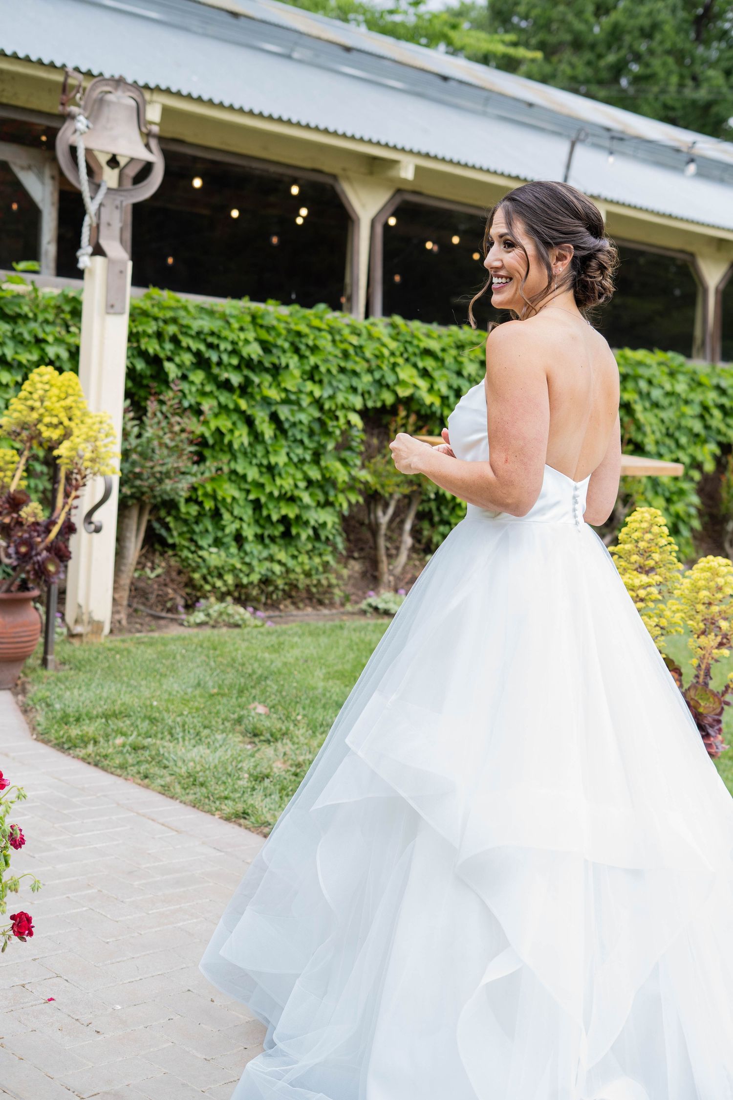 Bride in flowing white ballgown twirling on an outdoor patio with greenery backdrop.