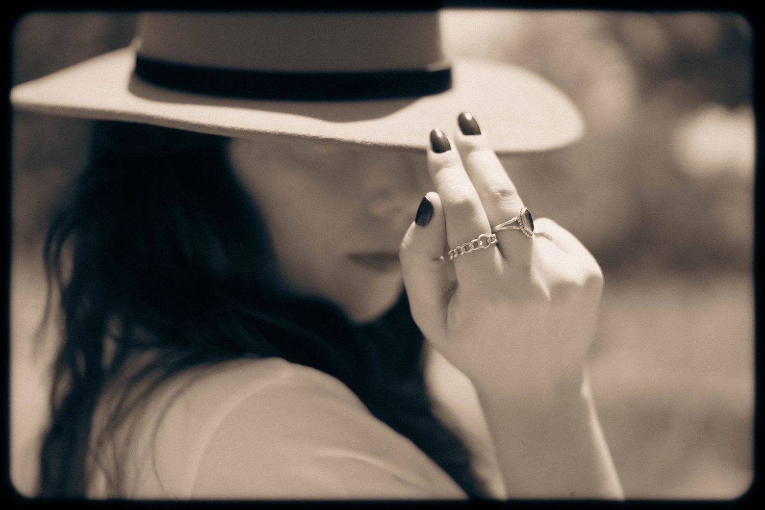 Artistic black and white portrait of someone in a wide brim hat showing rings on their hand.