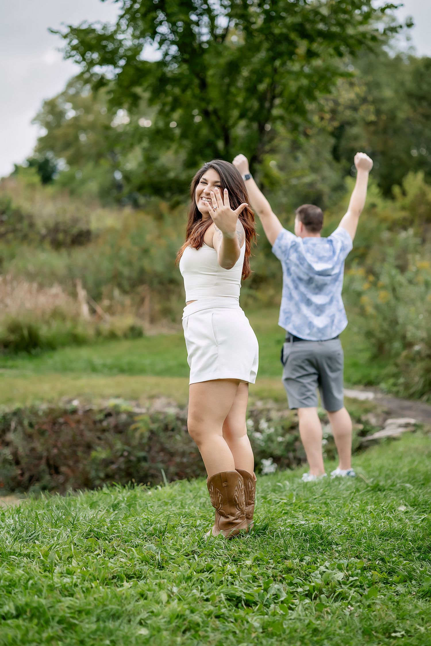Girl holding up her hand with engagement ring and man excited behind her
