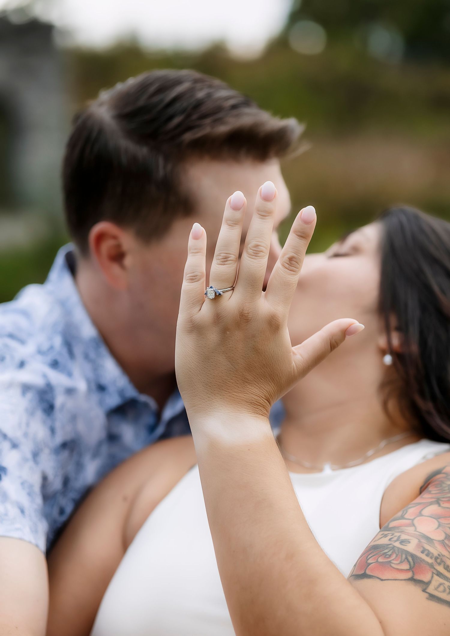 Woman holding up engagement ring while kissing fiancé