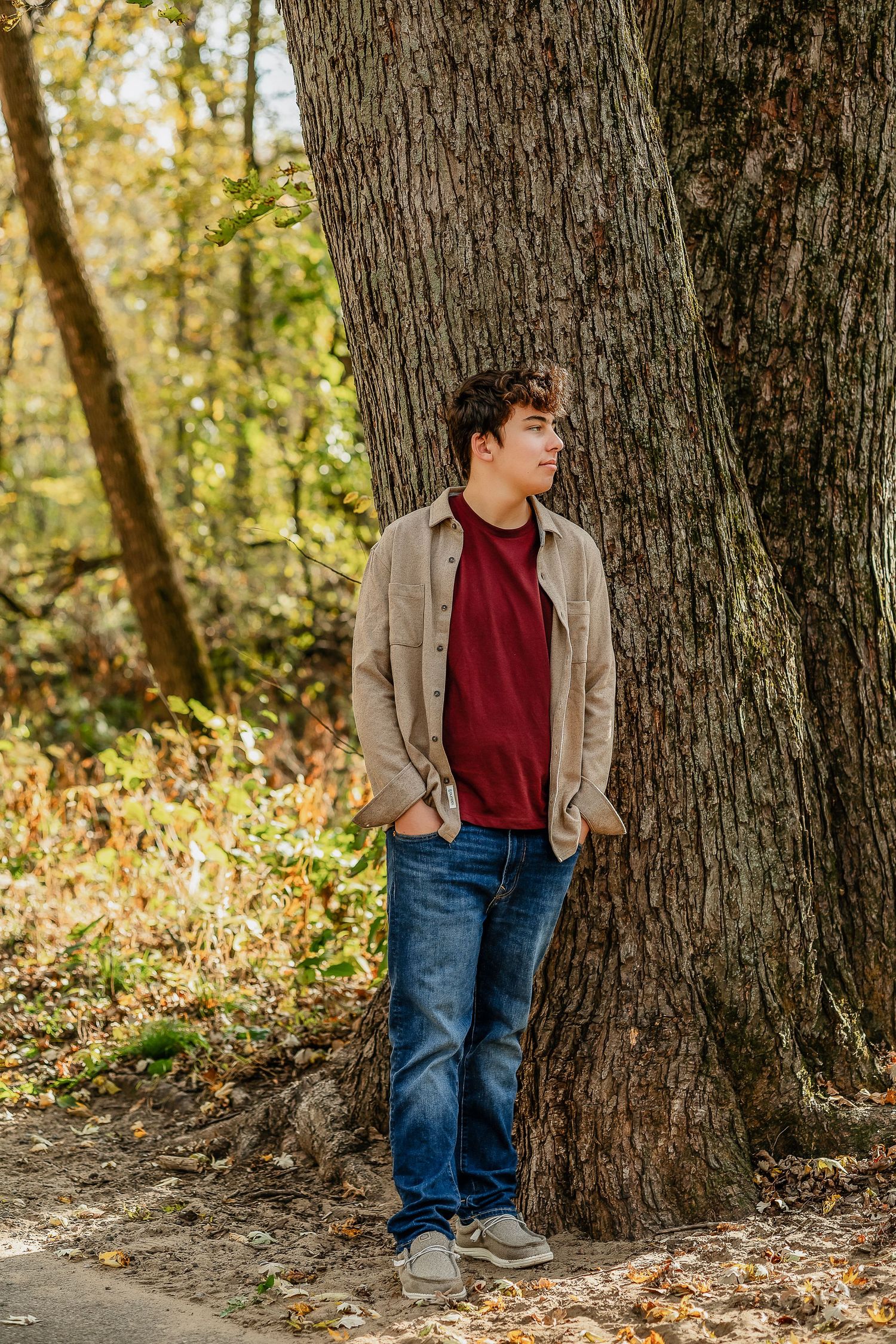 Boy with hands in his pocking looking sideways standing next to a tree