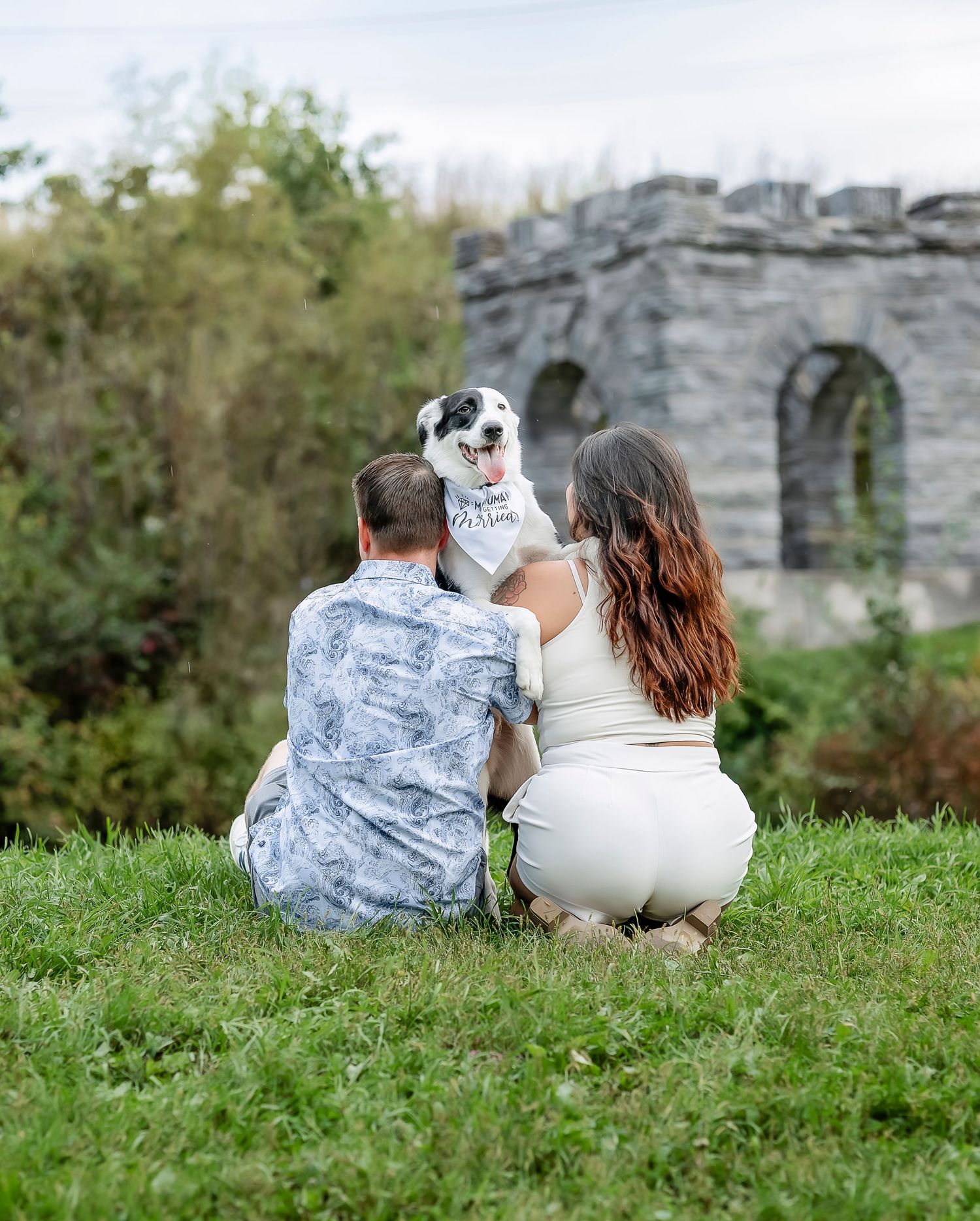 Couple sitting in the grass with their dog
