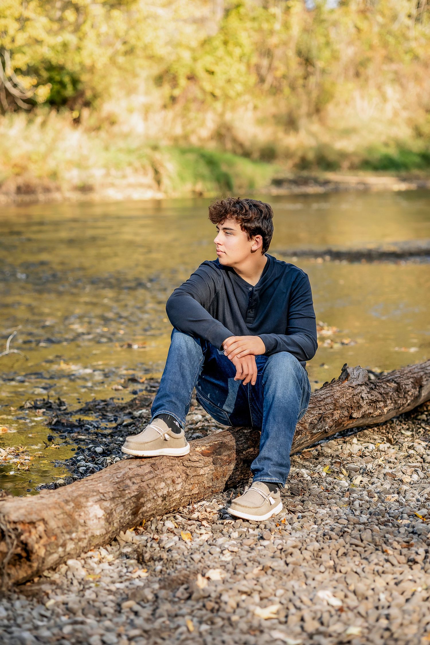 Young man looking out in the distance by the river, sitting on a log