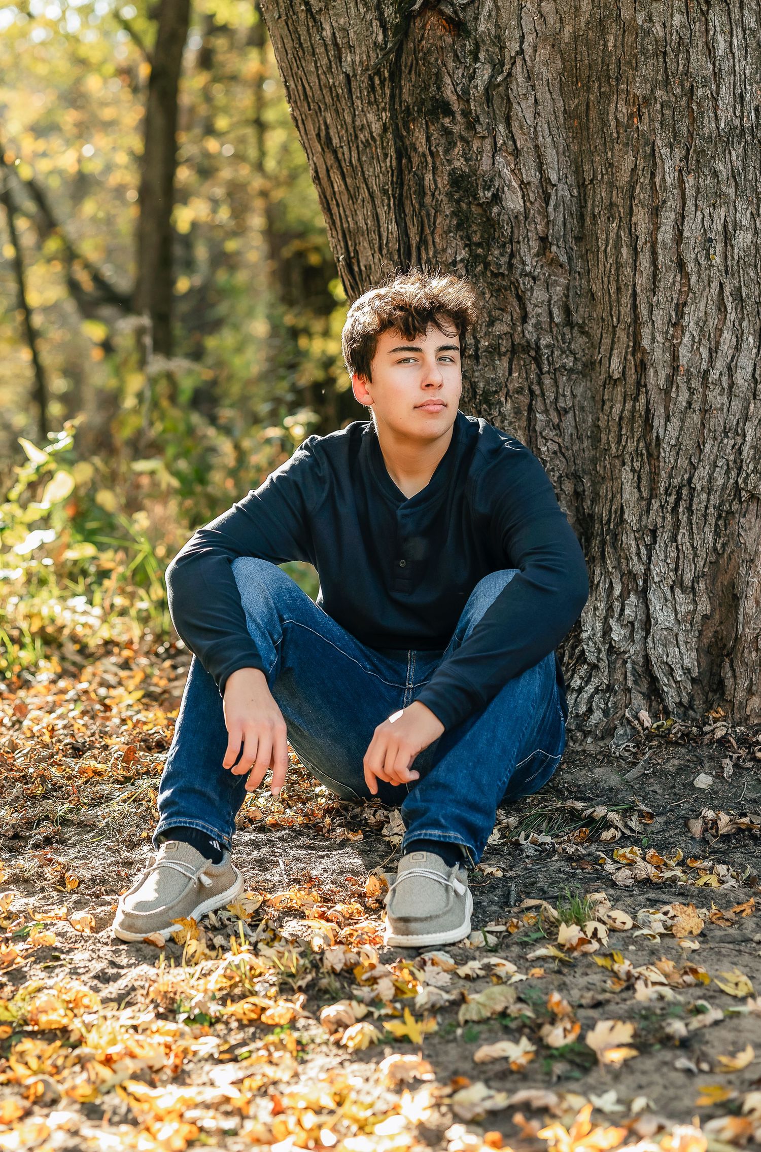 Young man wearing a black shirt and jeans near a tree in the woods