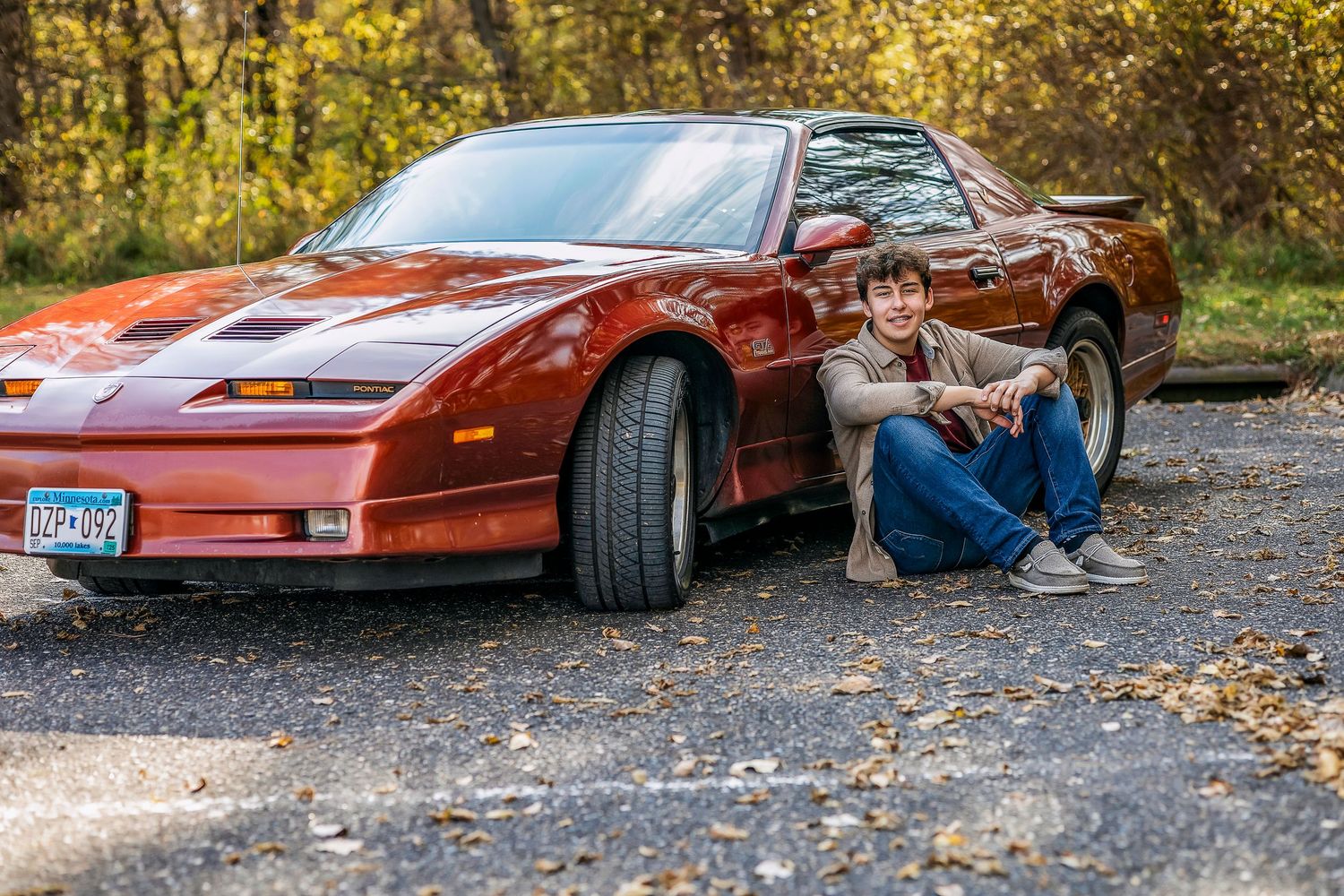 Boy sitting on the ground next to a red car
