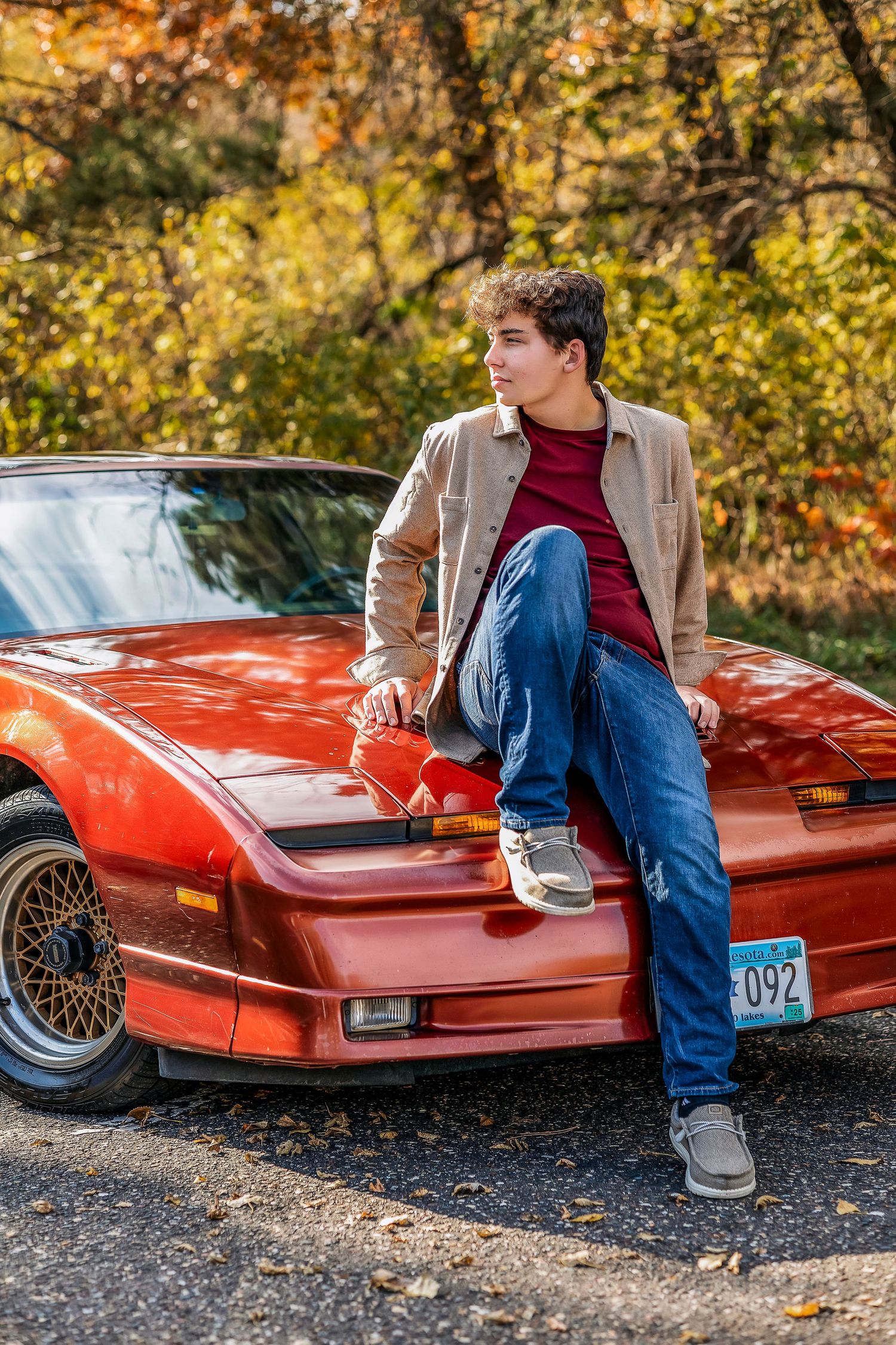 Young man with brown hair sitting on the hood of a red car