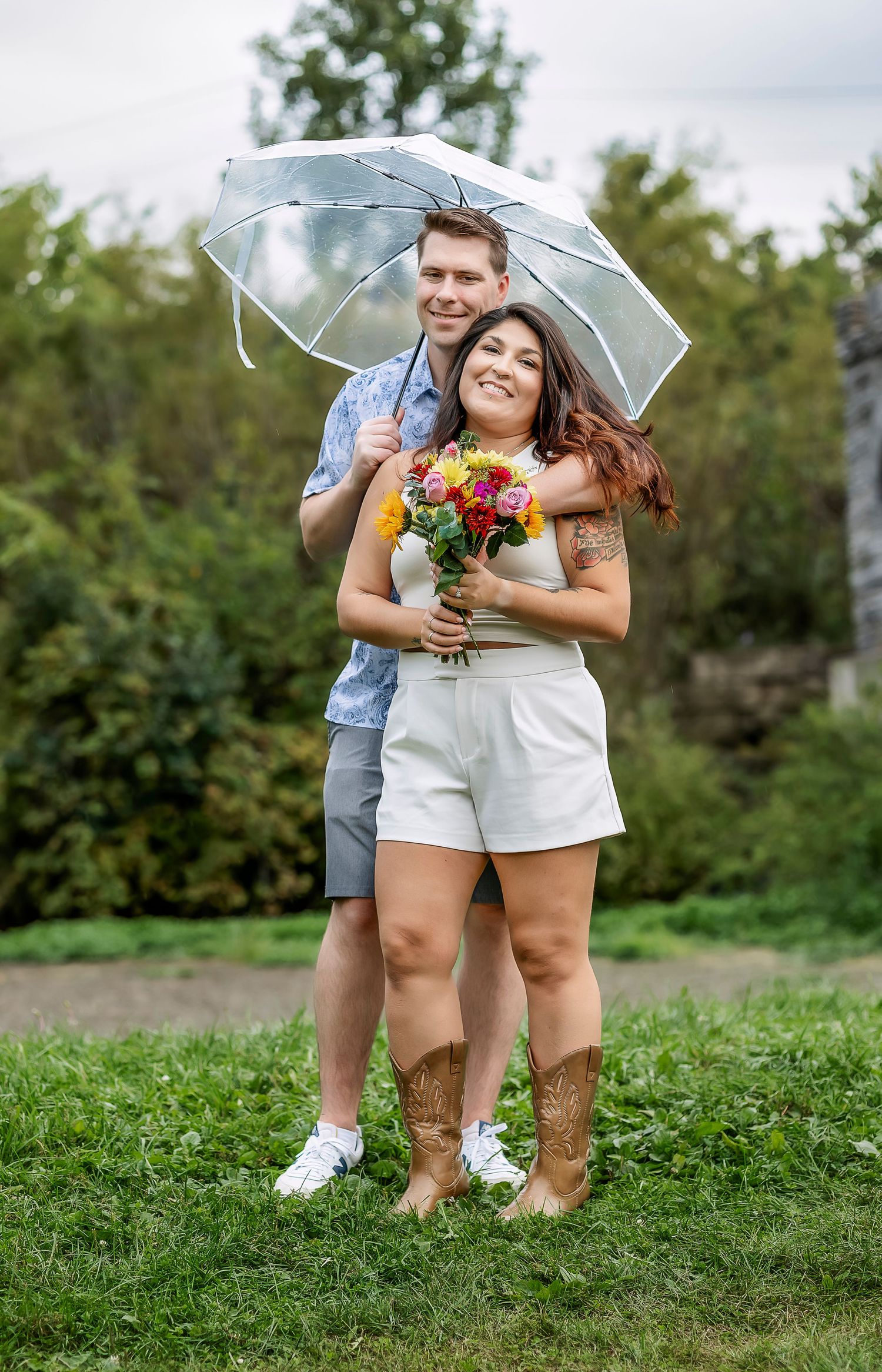 Couple standing with each other under umbrella holding flowers