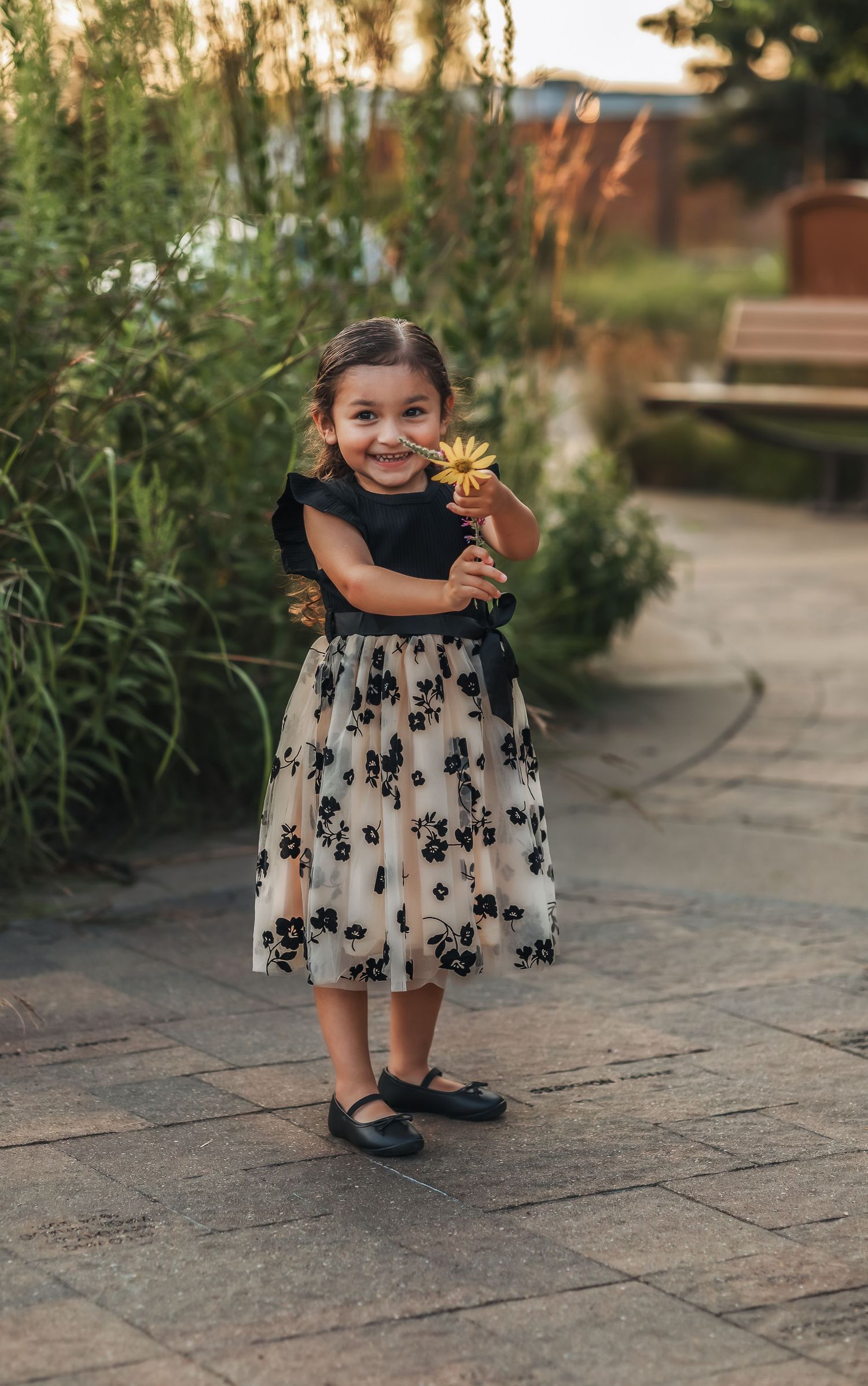 Small girl holding a yellow flower while smiling at the camera