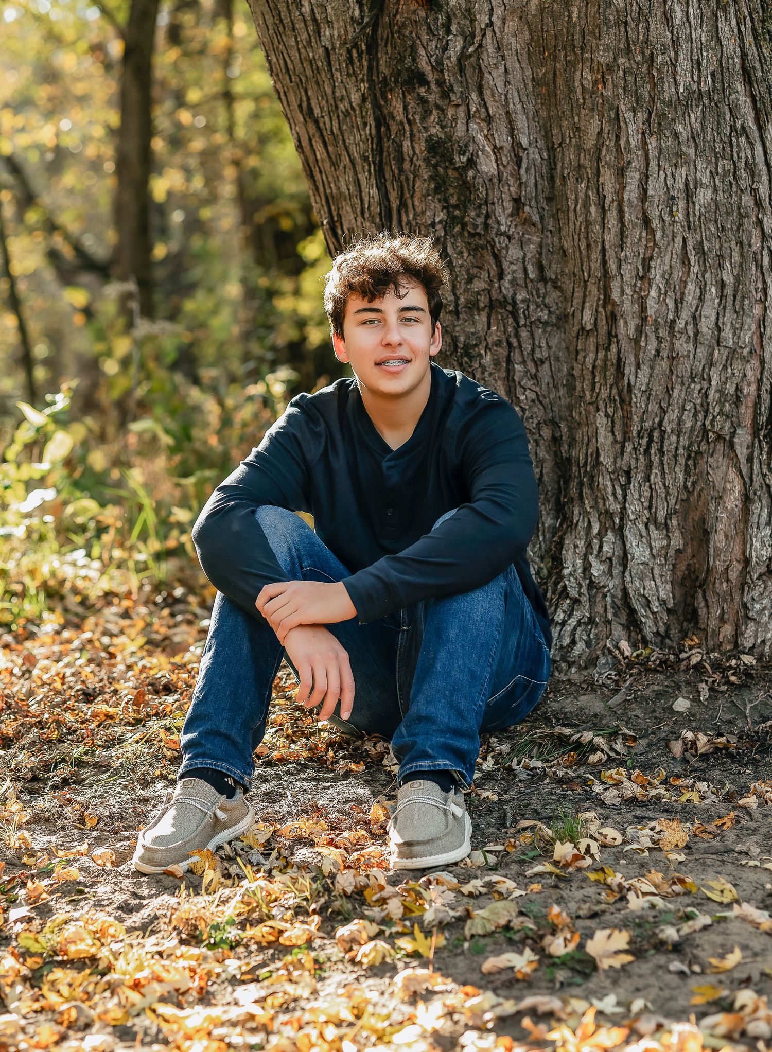 Boy wearing a black shirt and jean sitting near a tree