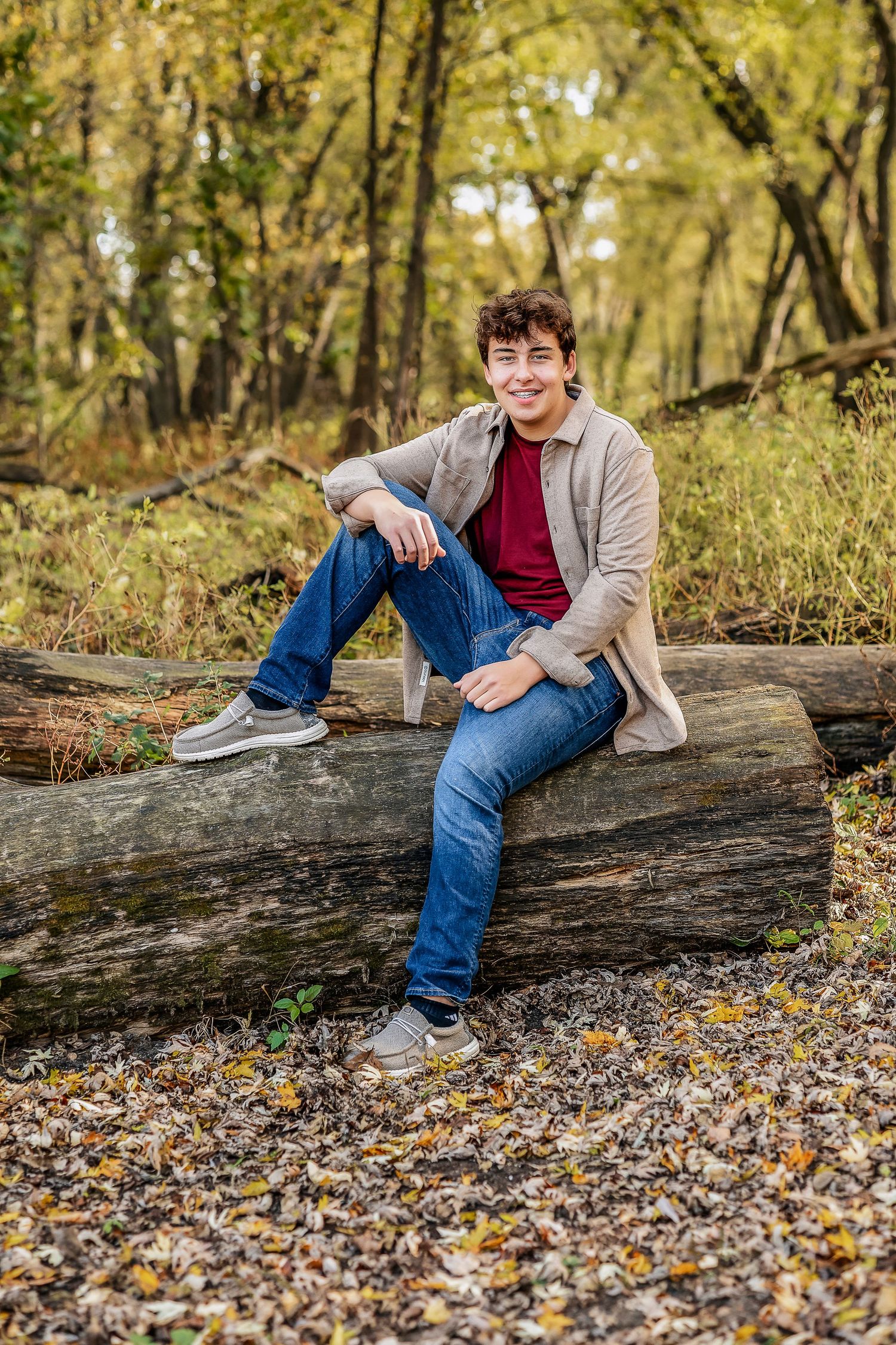 Boy in a red shirt and tan jacket sitting on a log