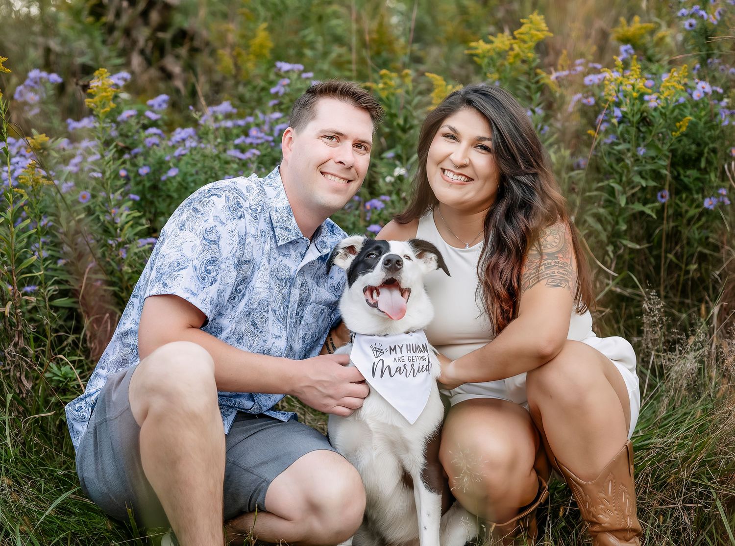 Couple crouching down next to a meadow with their dog