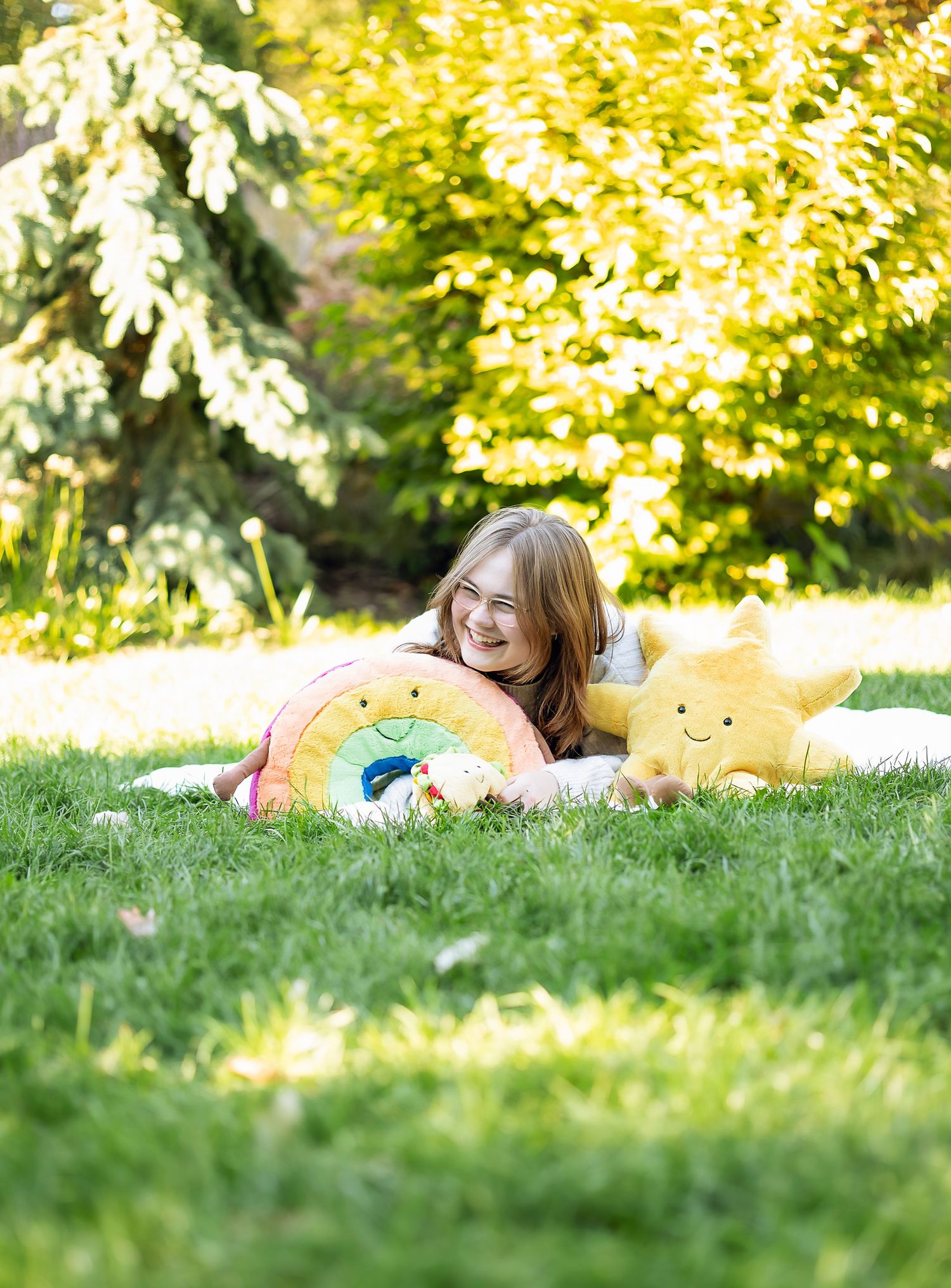 Girl laying in grass with stuffed rainbow and star