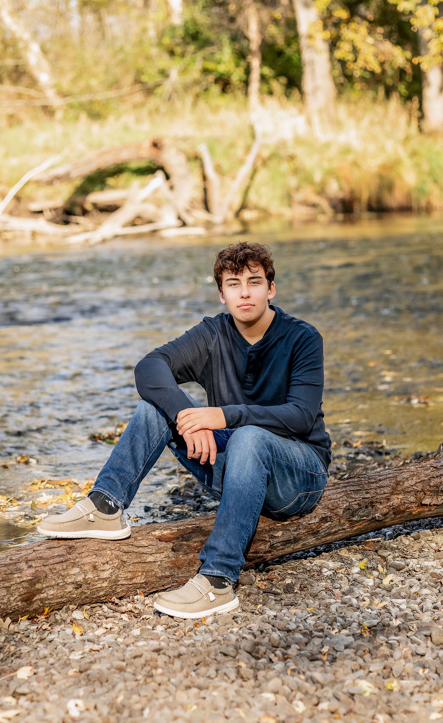 Man wearing a black shirt and sitting on a log by the river