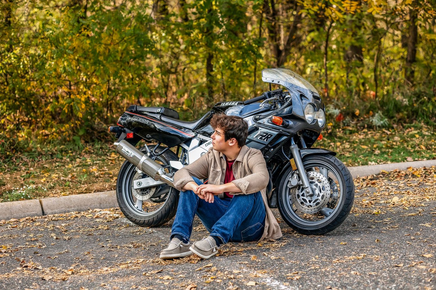 Boy looking out into the sky while sitting next to his motorcycle