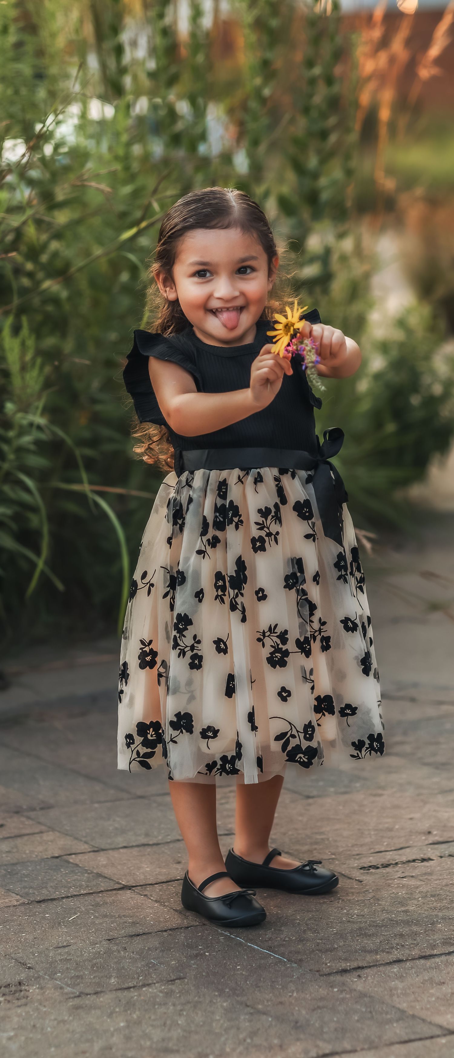 Little girl holding a yellow flower up in the air while smiling at the camera