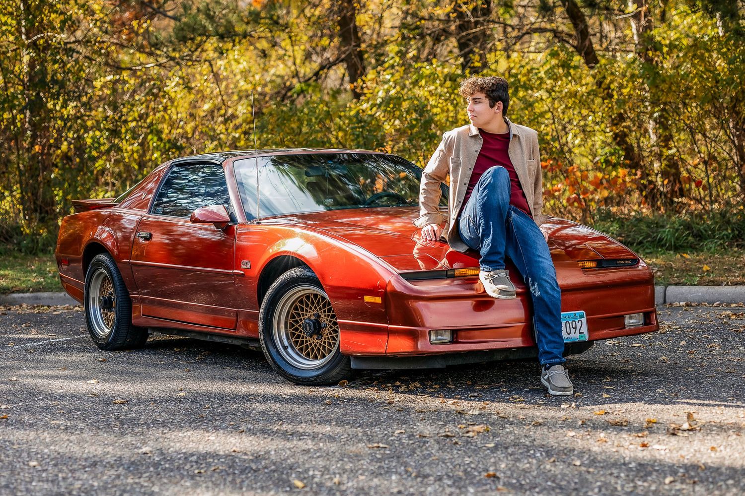 Full car view of young man wearing jean sitting on the hood of the car