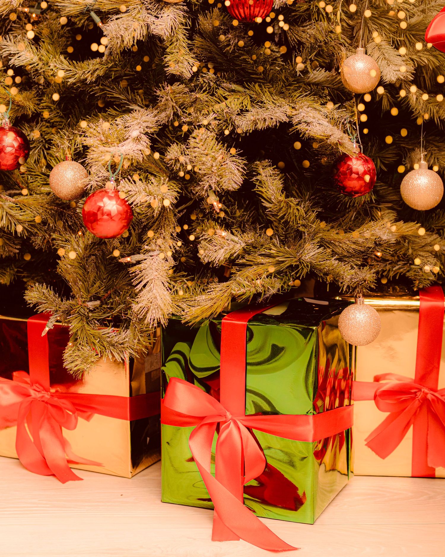 Colorful Christmas gifts with red ribbons under a decorated tree with red and gold ornaments.