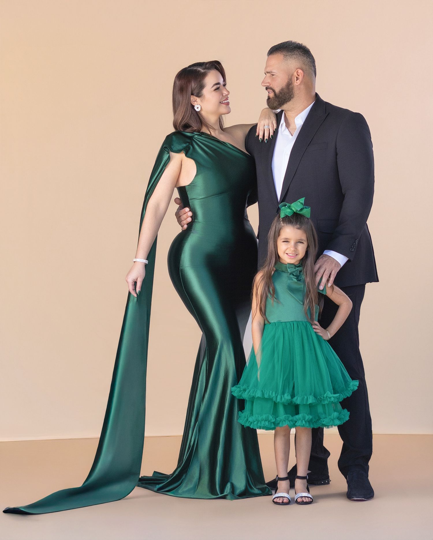 Family portrait with woman in emerald green gown, man in dark suit, and young girl in green dress posing together.