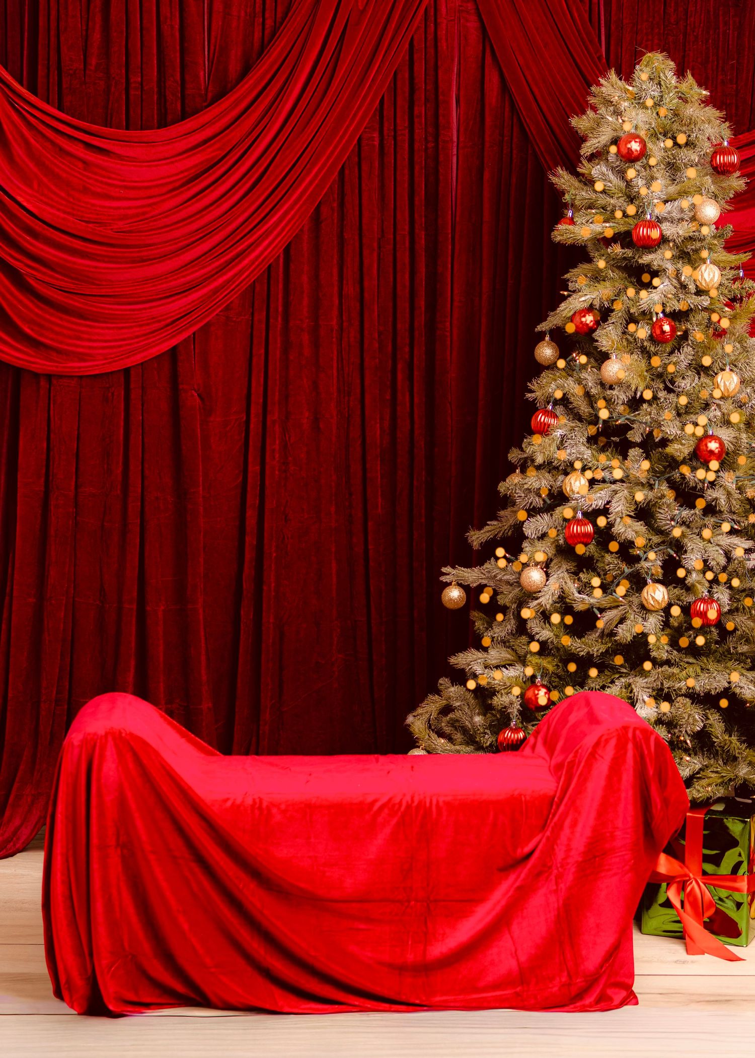 Red velvet curtains and draped sofa beside a decorated Christmas tree with red ornaments on a wooden floor.