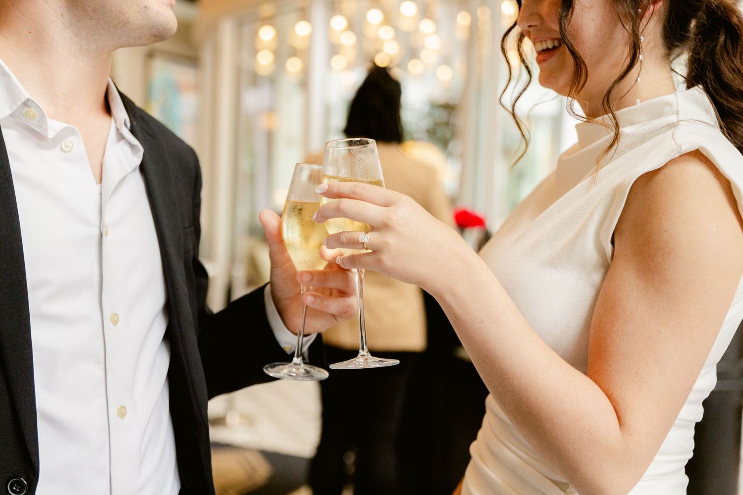 Two elegantly dressed people toast with champagne flutes during a formal celebration at an indoor venue.