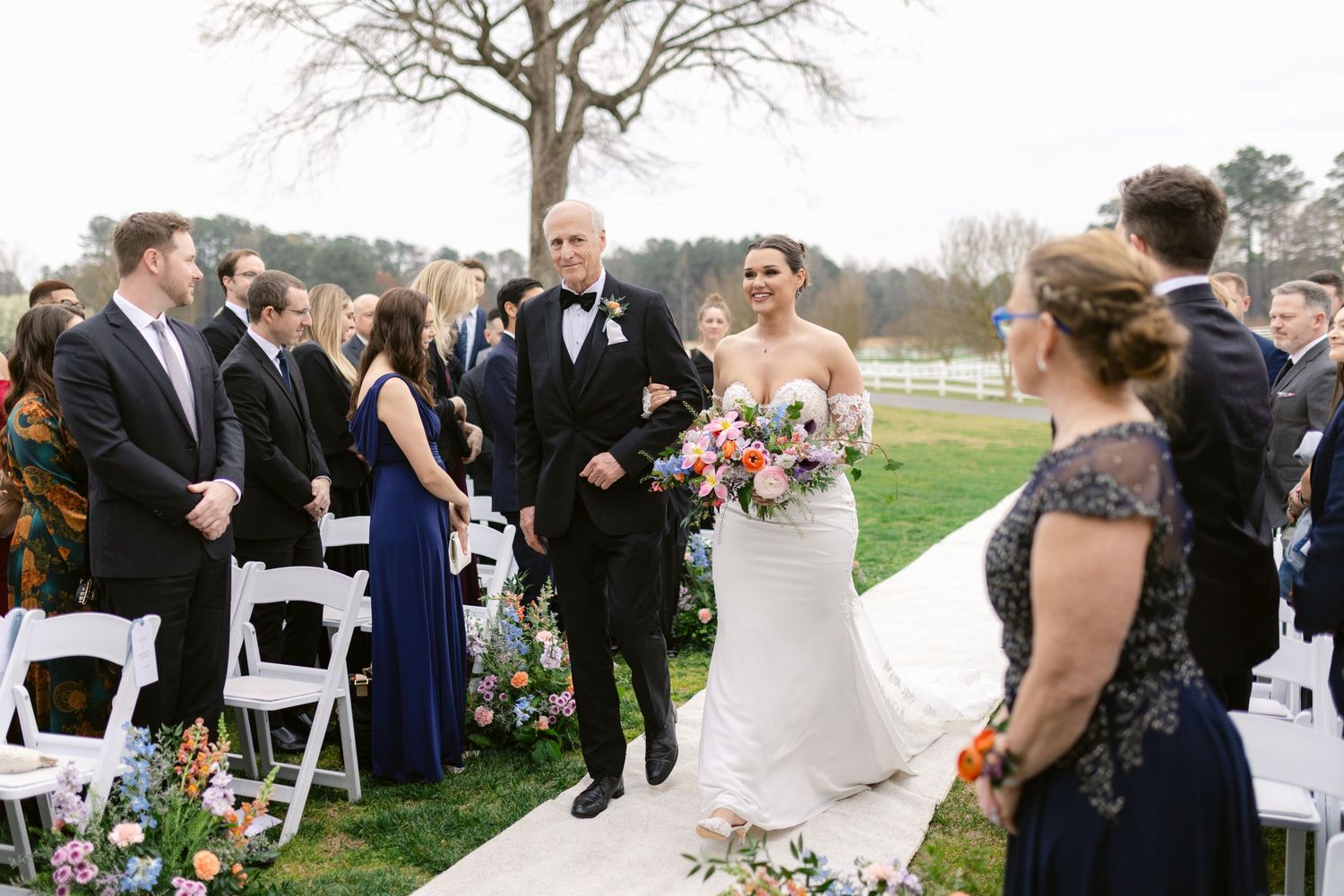Wedding ceremony celebration outdoors with decorated aisle and white chairs on a grassy lawn.