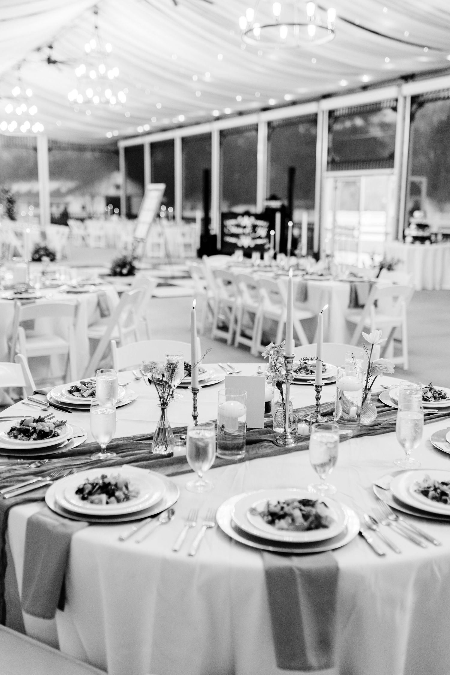 Elegant wedding reception setup with round tables, white linens and crystal chandeliers in a draped ceiling venue.