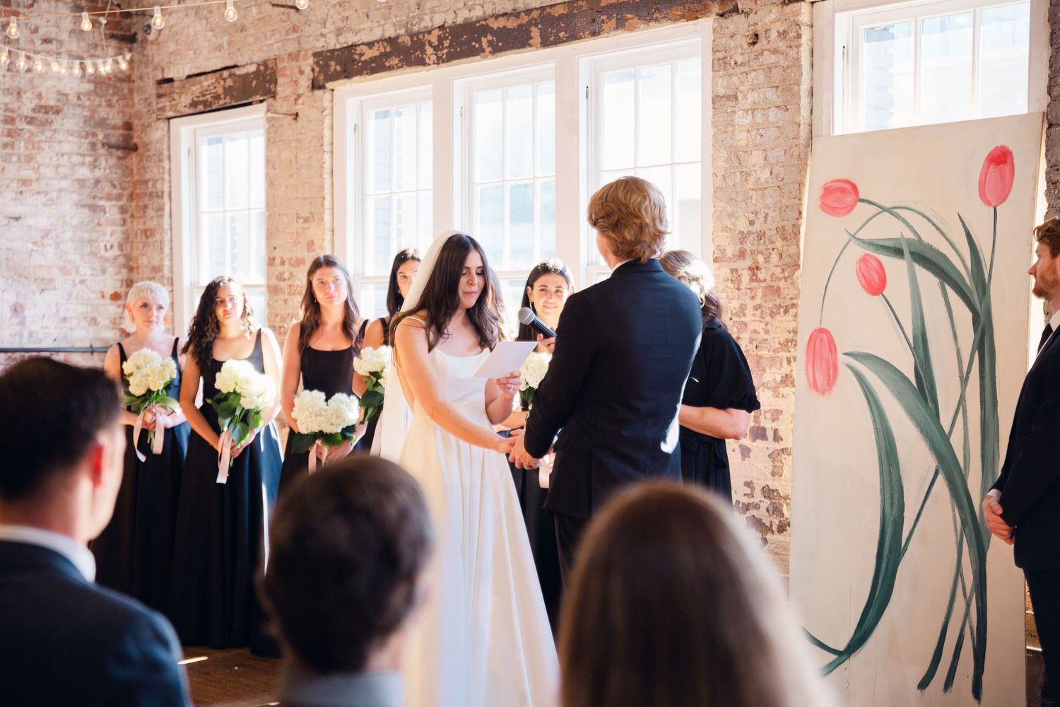 A wedding ceremony taking place in an industrial-style venue with exposed brick walls and large windows.