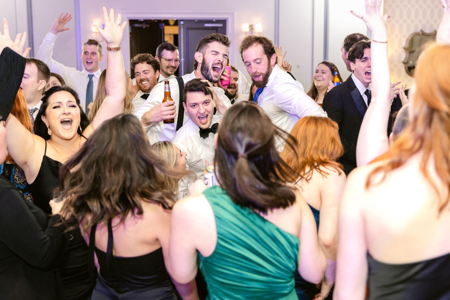 Wedding guests dance and celebrate together on a crowded dance floor during a lively reception party.