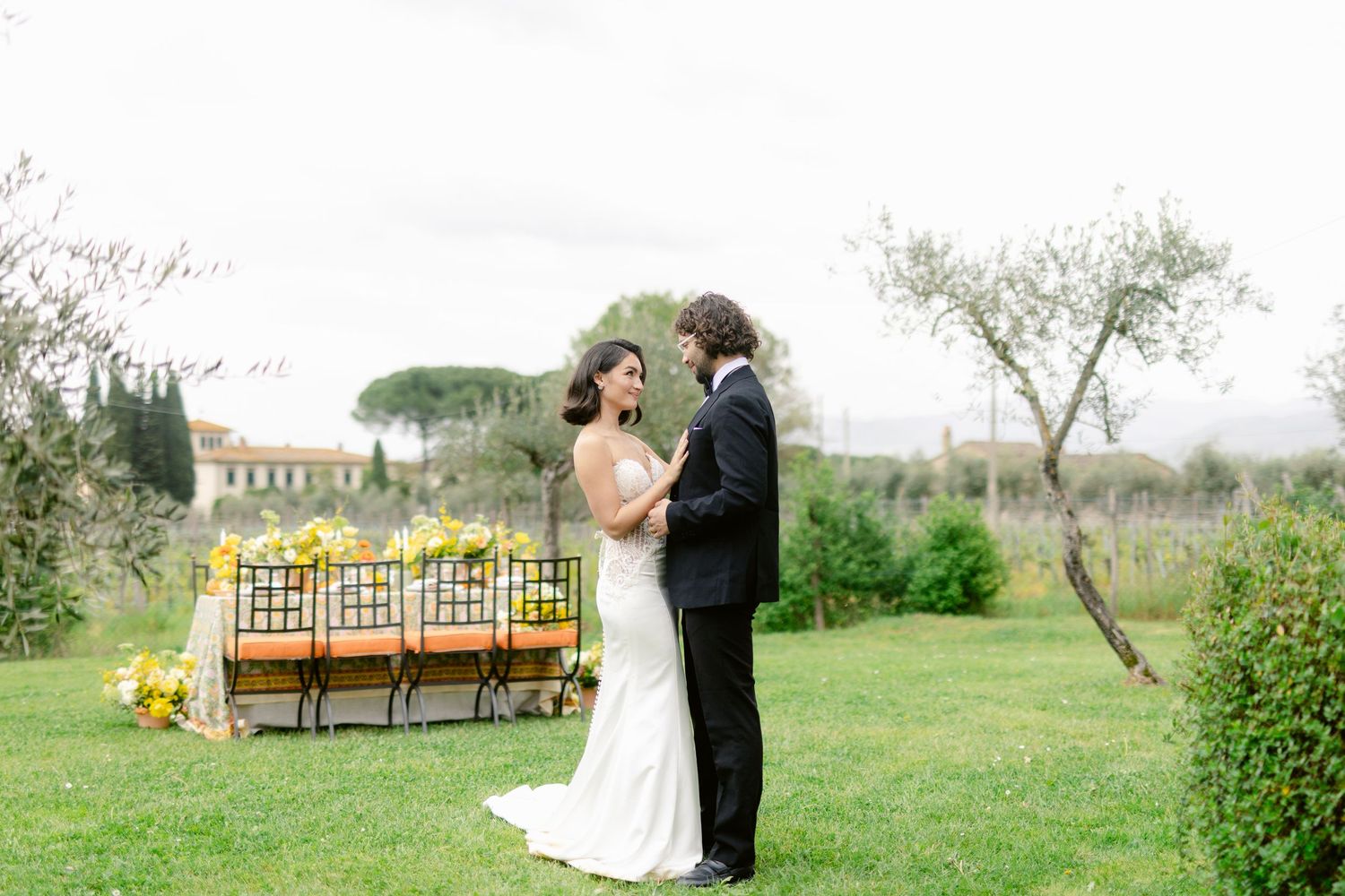 A romantic outdoor wedding ceremony setup with wooden benches and yellow sunflowers in a lush garden setting.