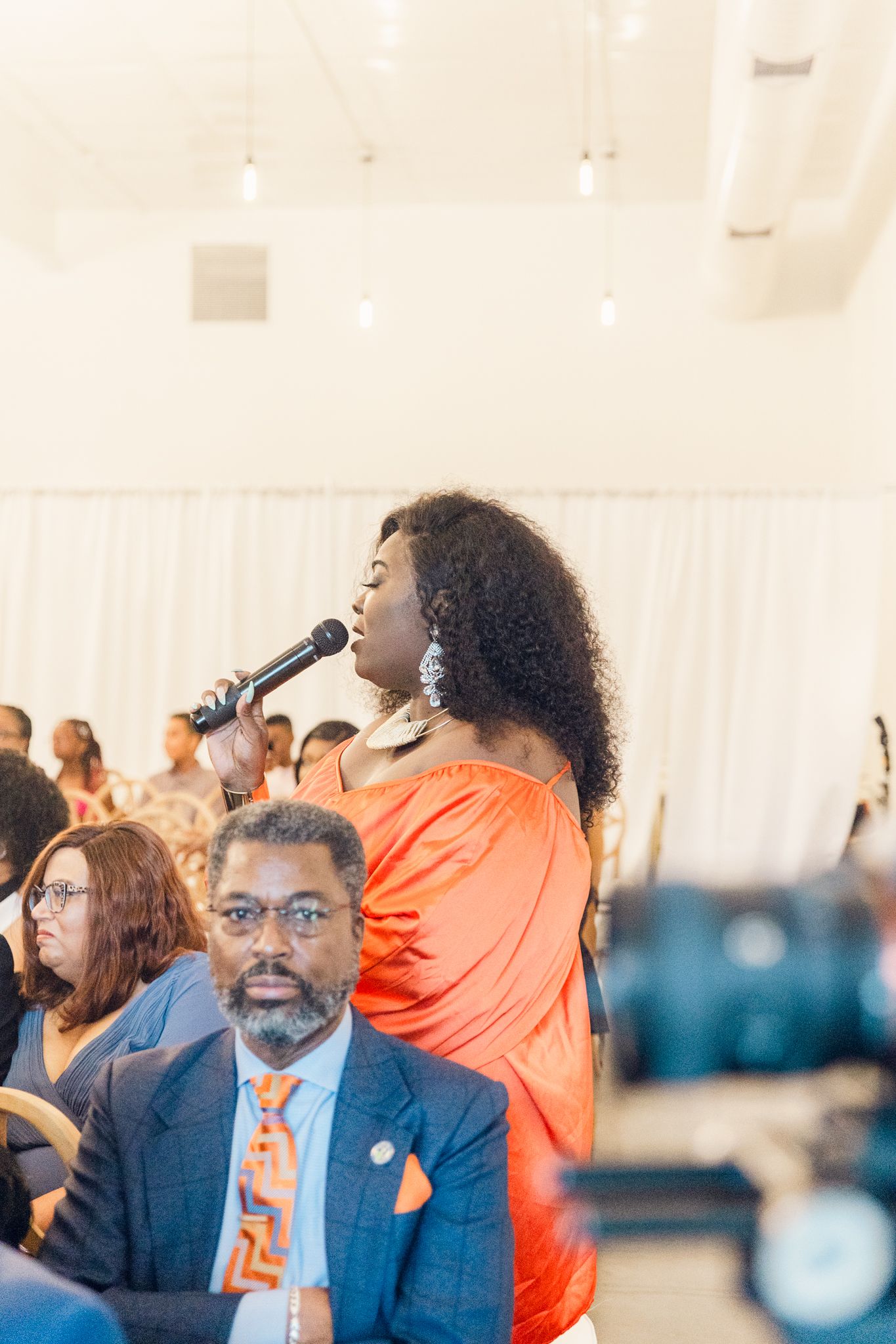 Wedding guests in orange and blue attire gather at an indoor celebration event.