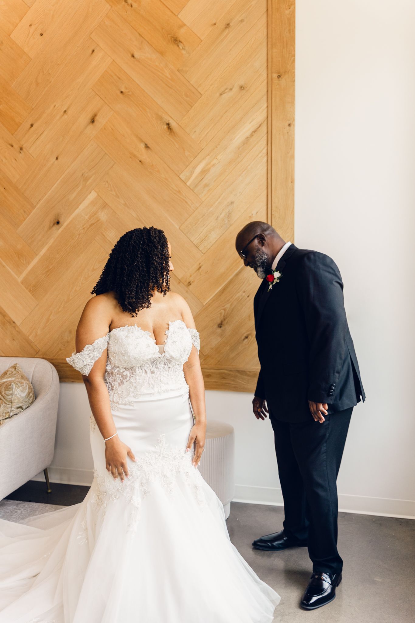 A couple shares a sweet first look moment before their wedding ceremony against a light wooden herringbone wall.