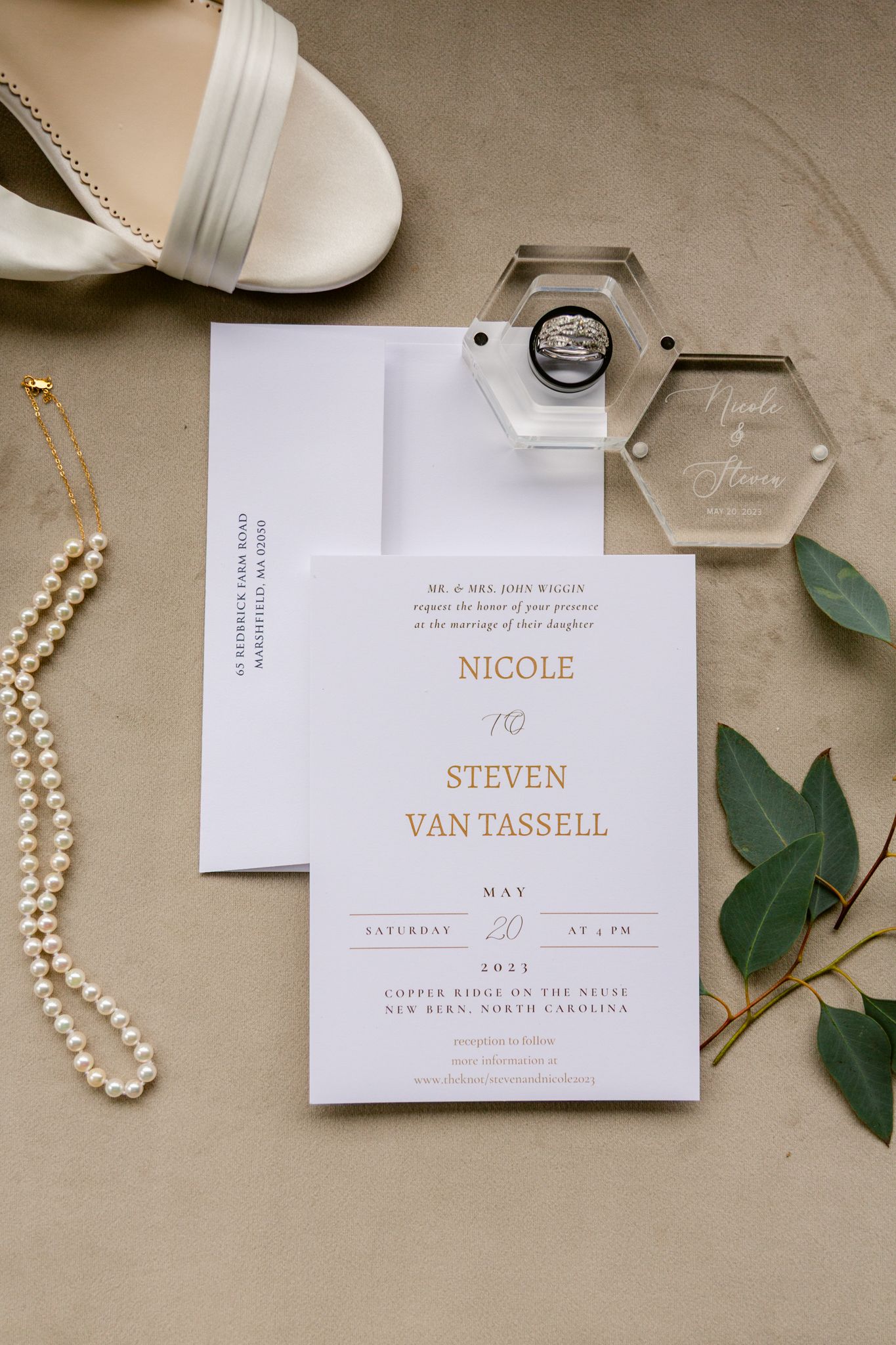Wedding invitation suite with elegant typography, pearl necklace, and eucalyptus leaves arranged on beige background.