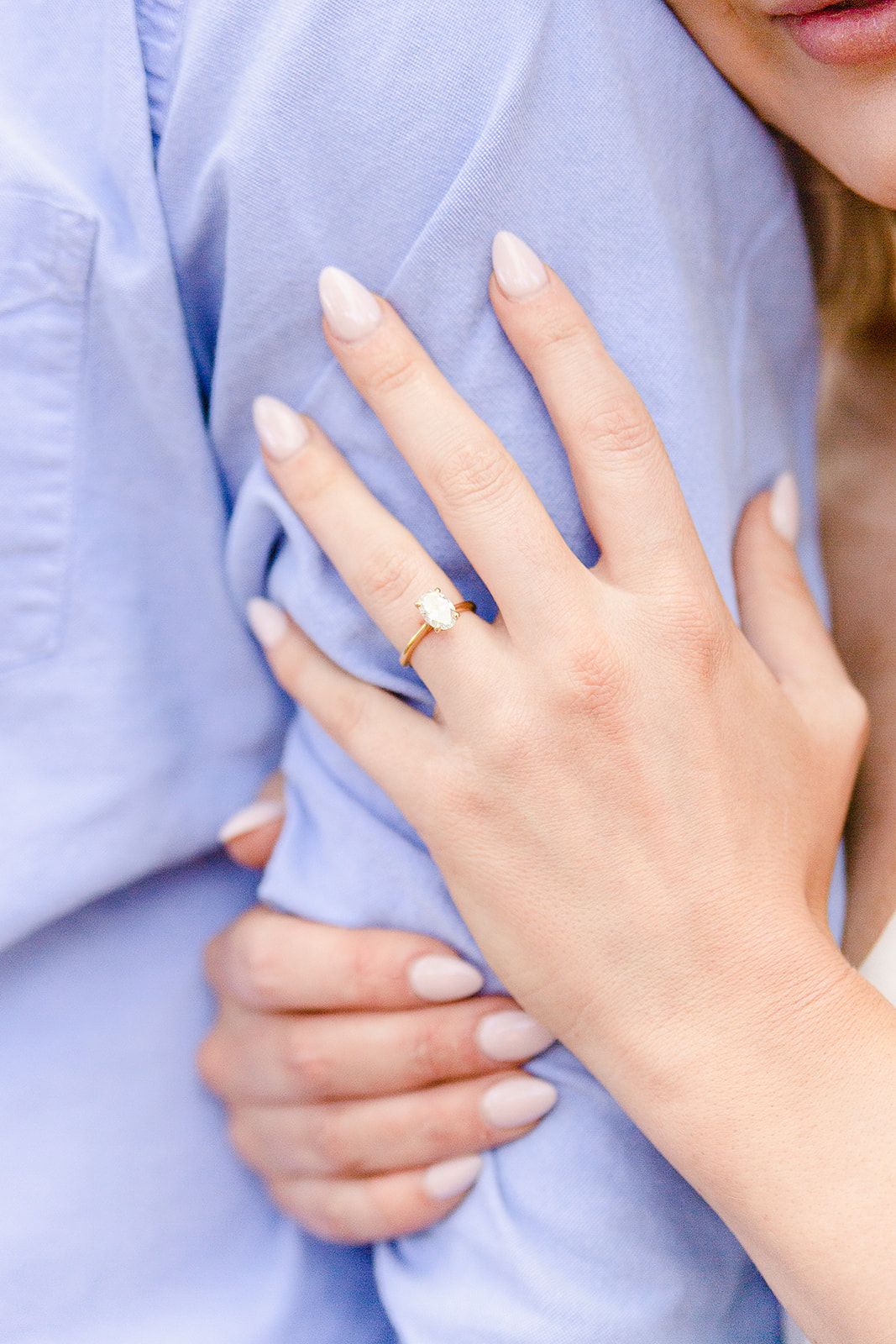 Close-up of hands showing engagement ring on finger against light blue fabric background.
