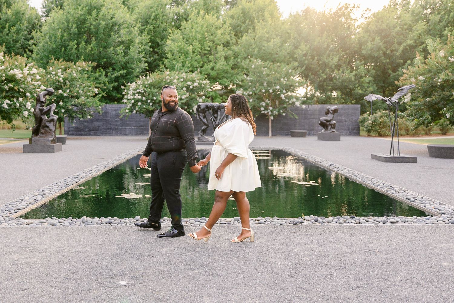 Two people stand together near a reflecting pool in a garden setting during golden hour.