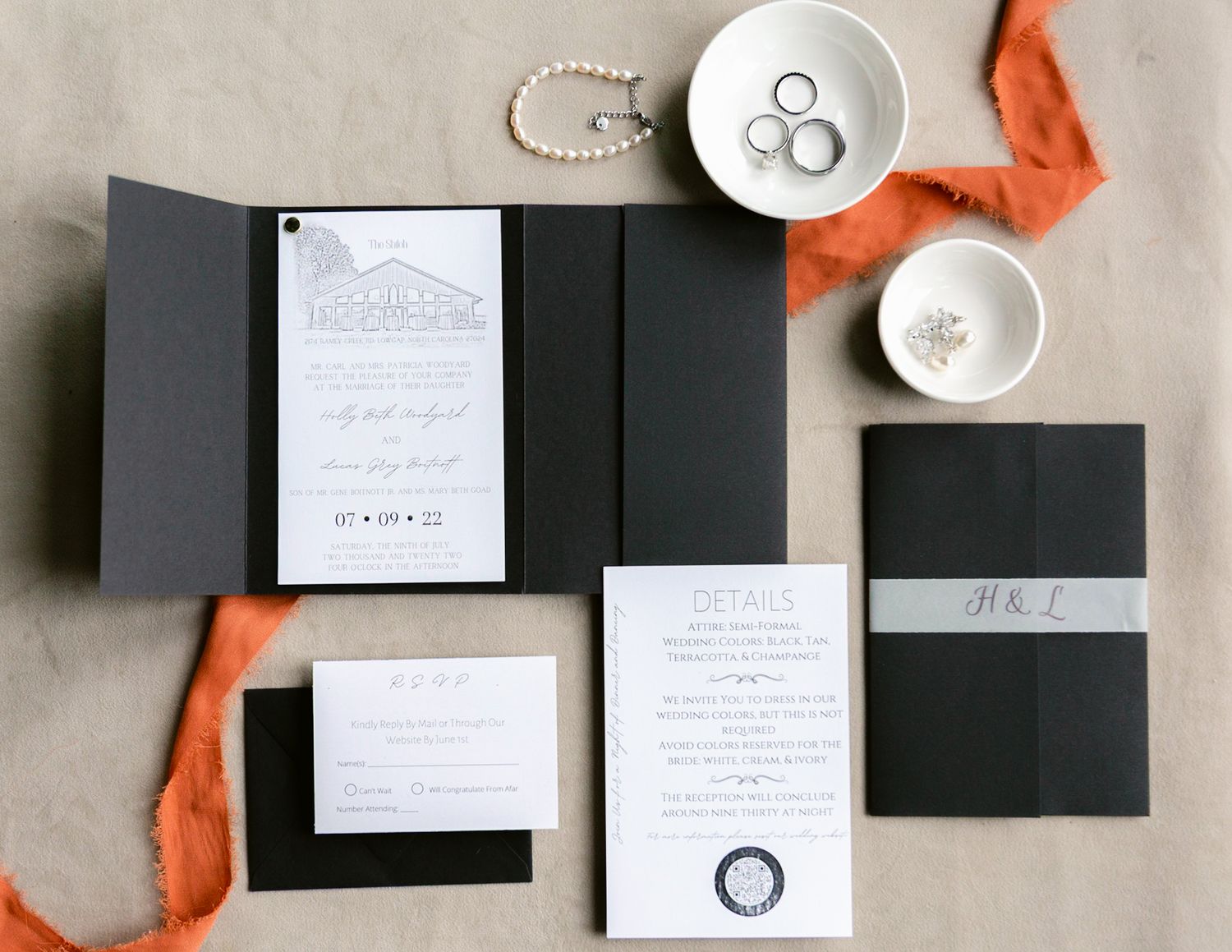 Elegant black and white wedding invitation suite with coral ribbon and silver rings on neutral background.