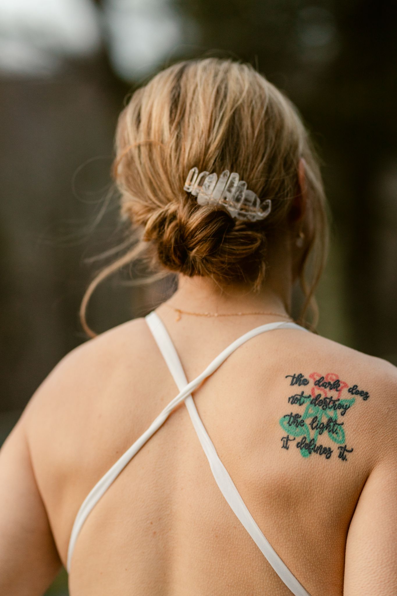 Close-up of an elegant bridal updo with crystal hair clip and visible back tattoo.