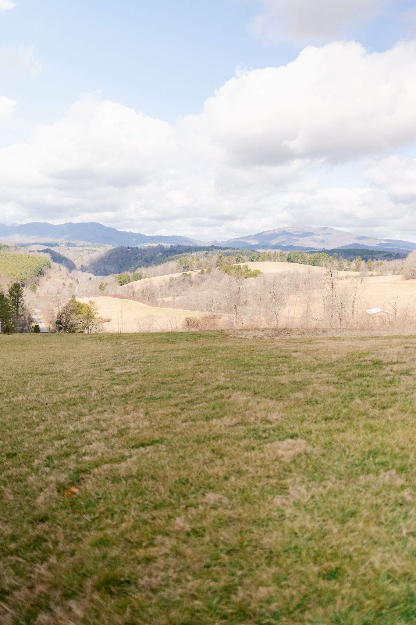 Rolling green hills and mountains stretch across the landscape under partly cloudy skies in a rural countryside setting.